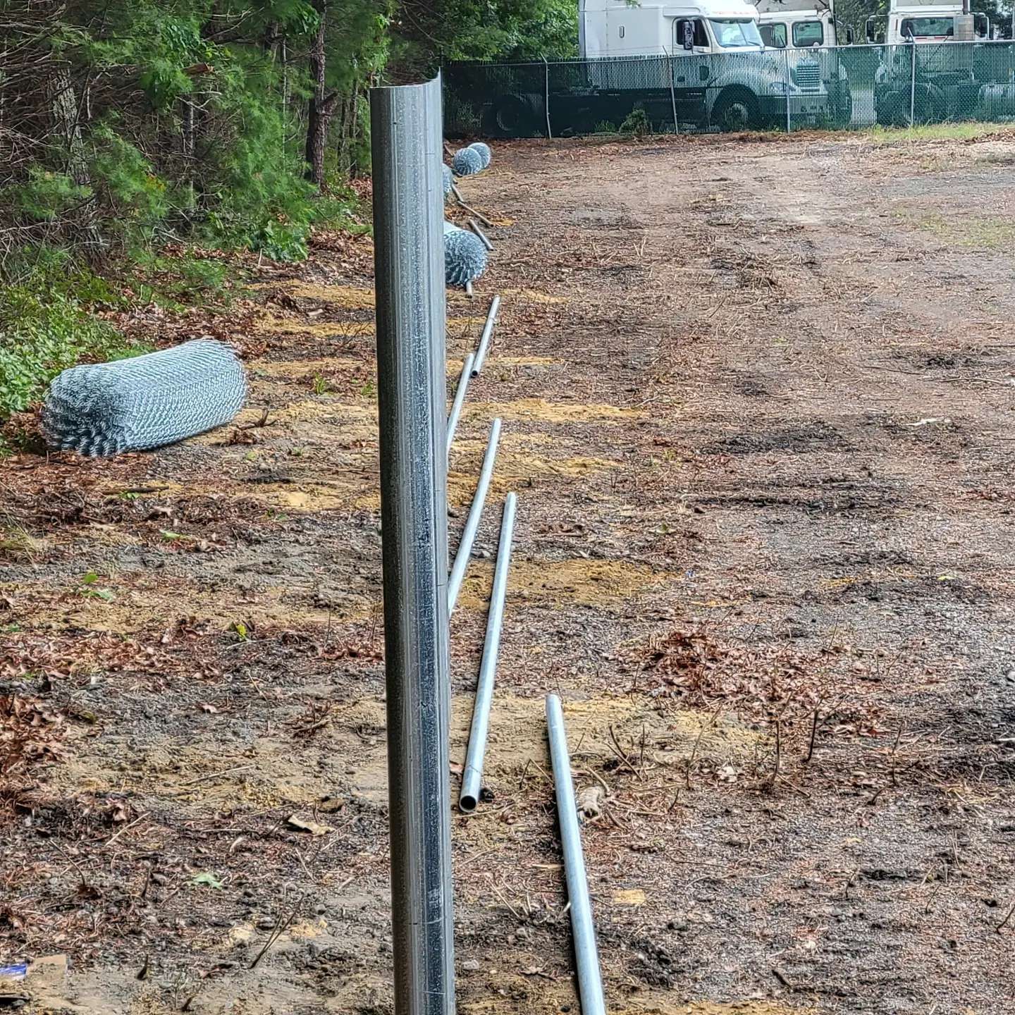 Fence posts and wire in a muddy field, with a forest in the background.