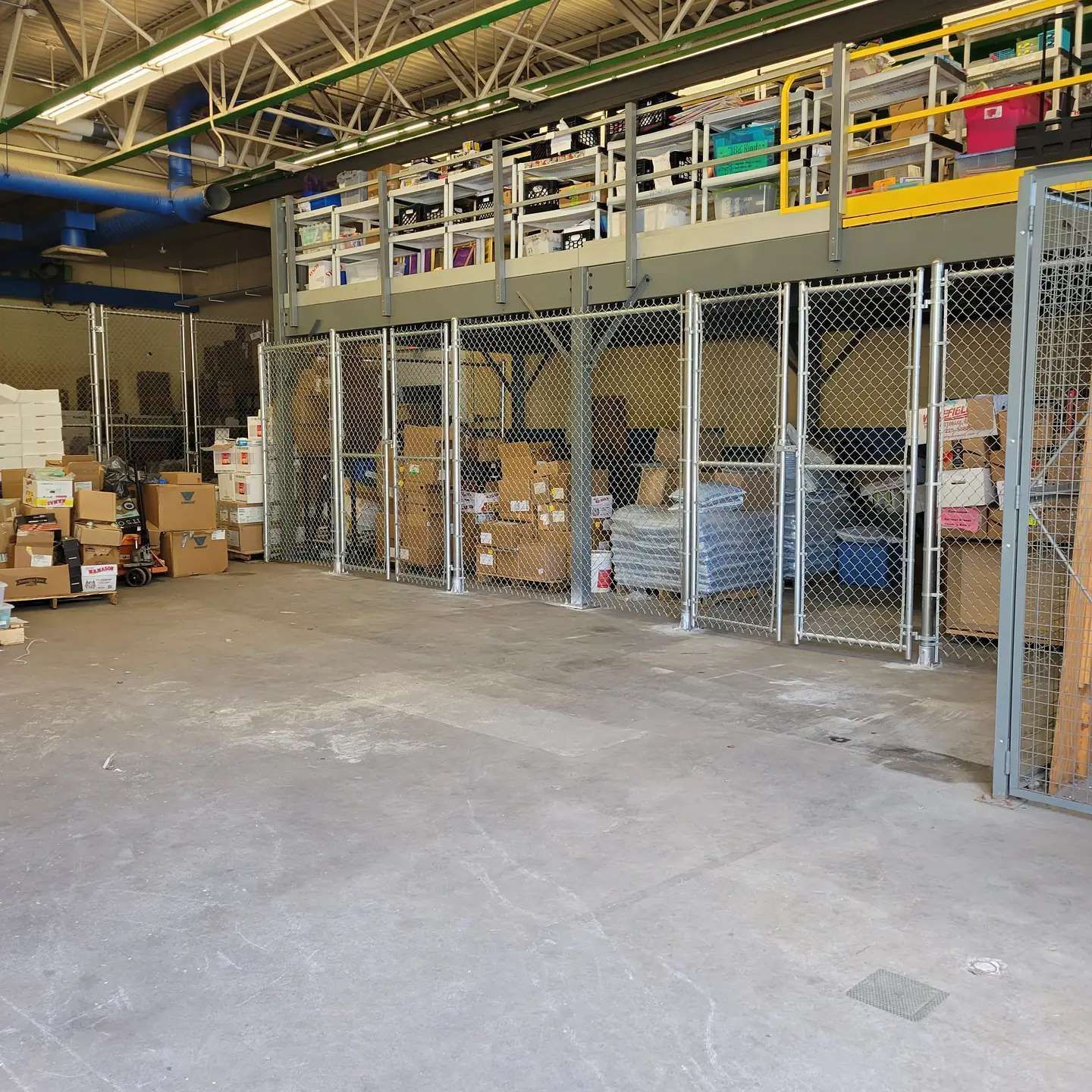 Warehouse interior with chain-link fenced storage areas containing boxes, with a mezzanine level.