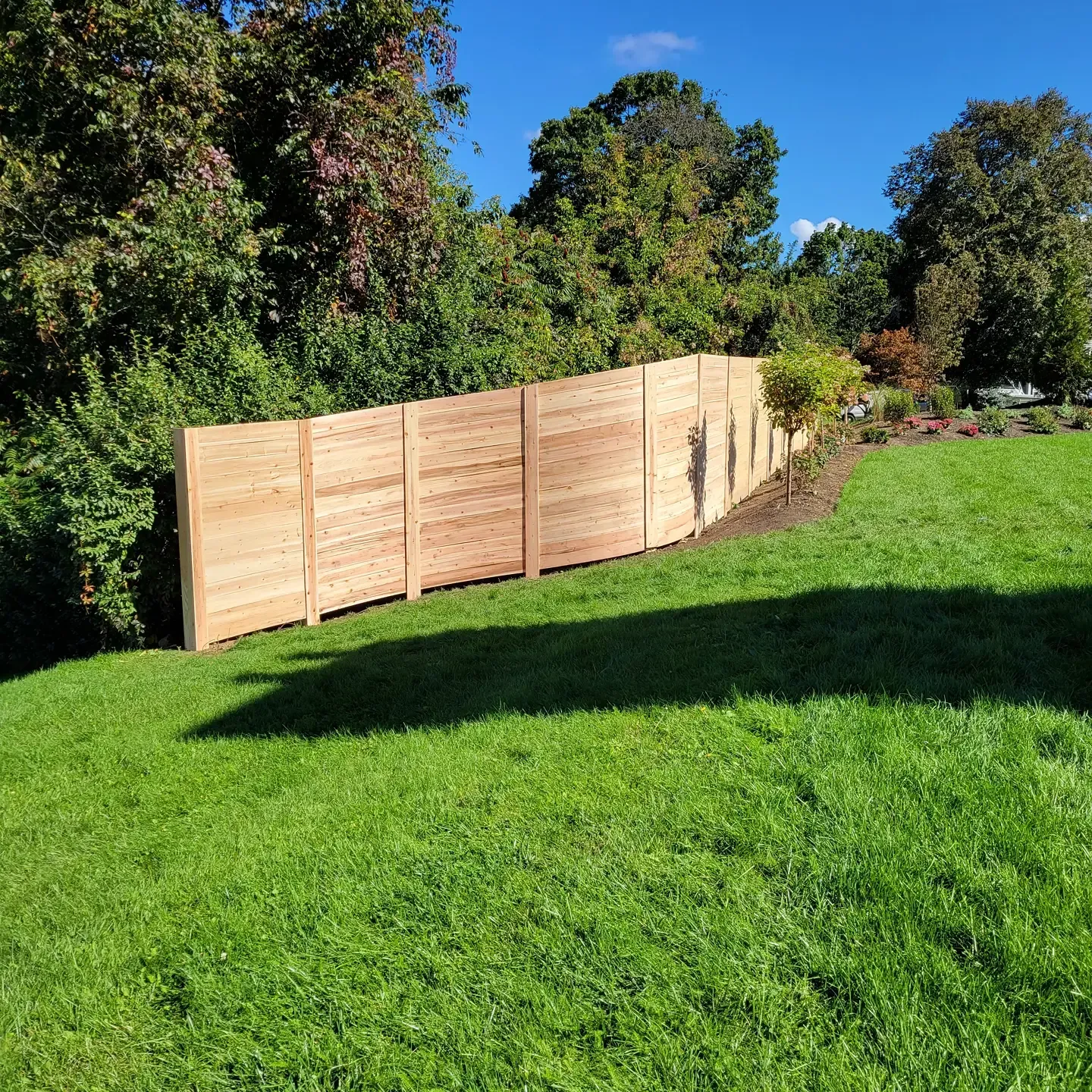 Wooden fence on a green lawn, trees in the background under a blue sky.