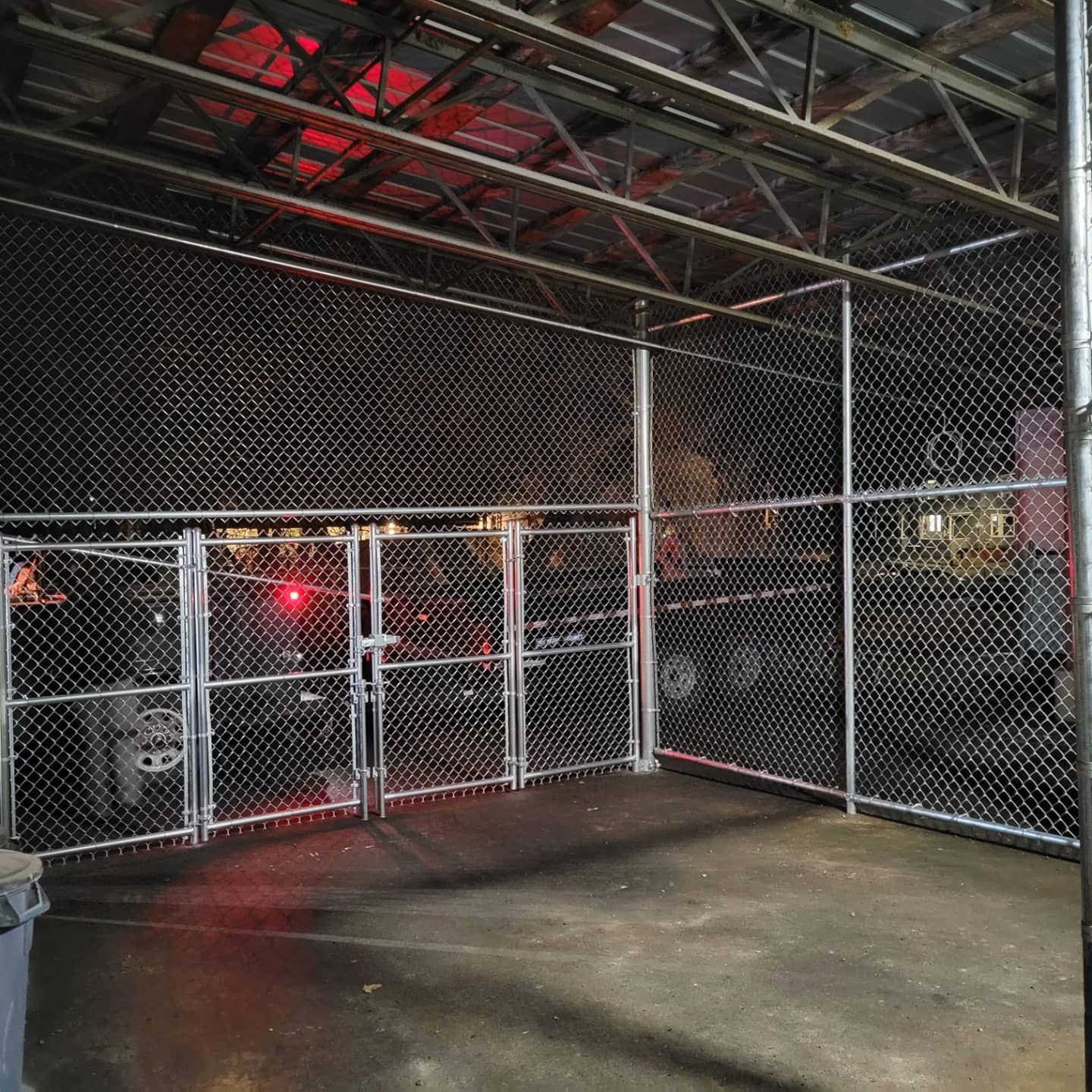 Chain link fence enclosure inside a warehouse. Steel supports, gray concrete floor. Dim lighting.
