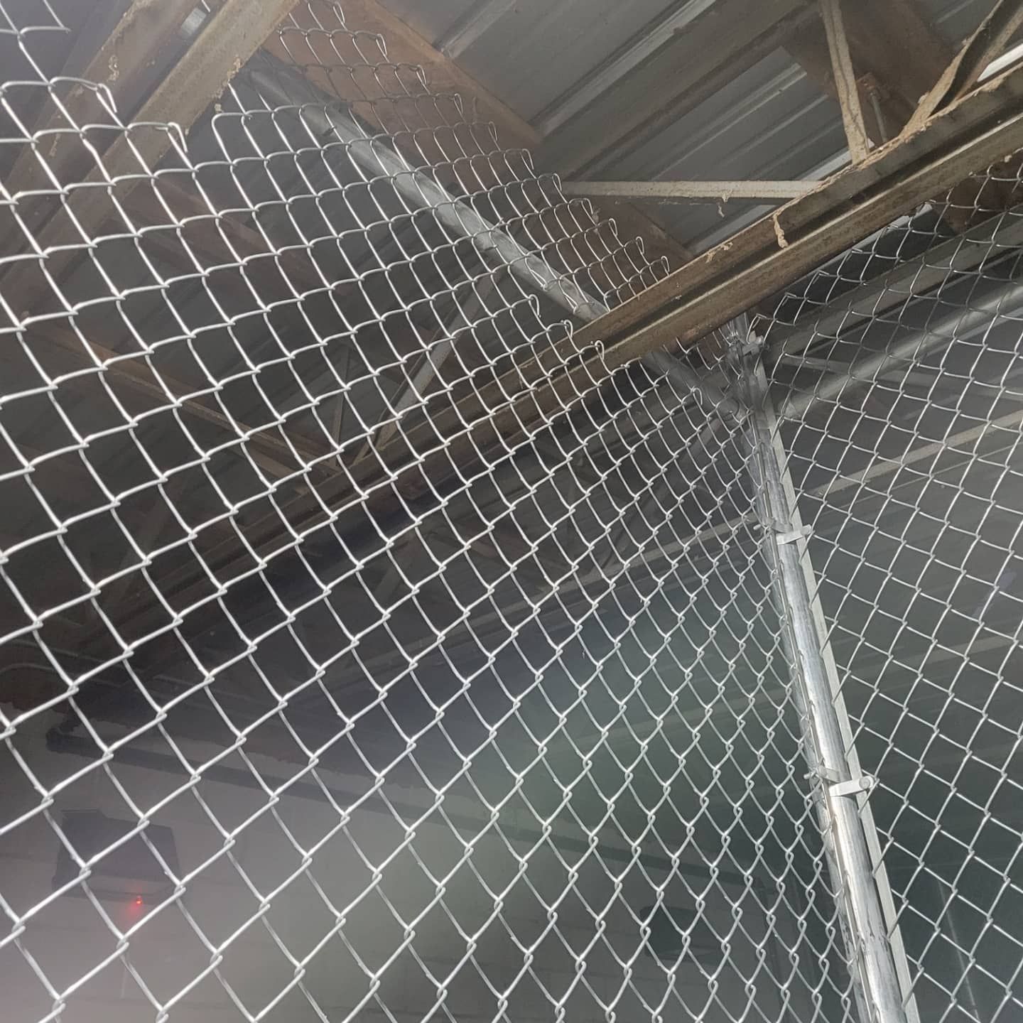 Chain-link fence attached to a wooden structure, forming a partial enclosure. Inside a metal building.