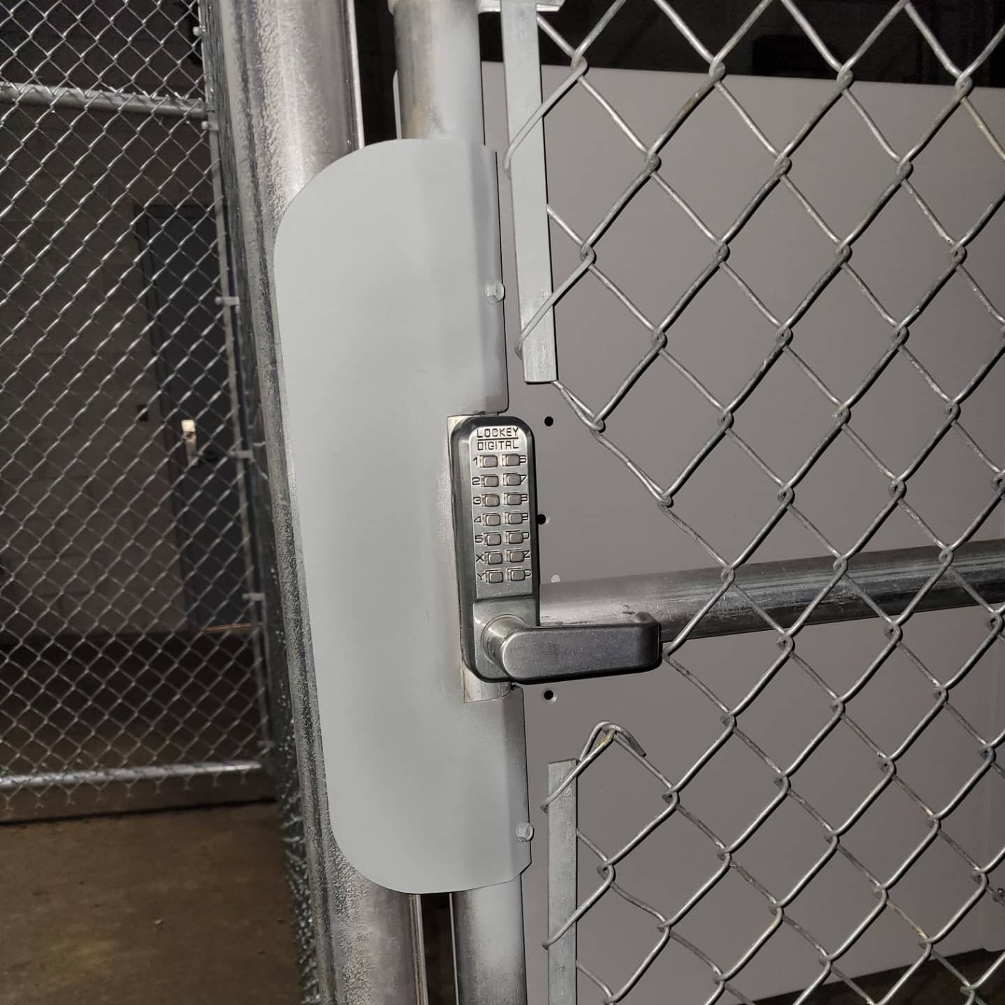 Chain link gate with digital keypad lock, gray metal, industrial setting.