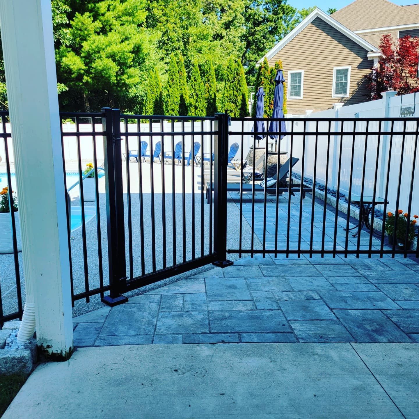 Black metal gate in a patio, with a pool visible through the fence.