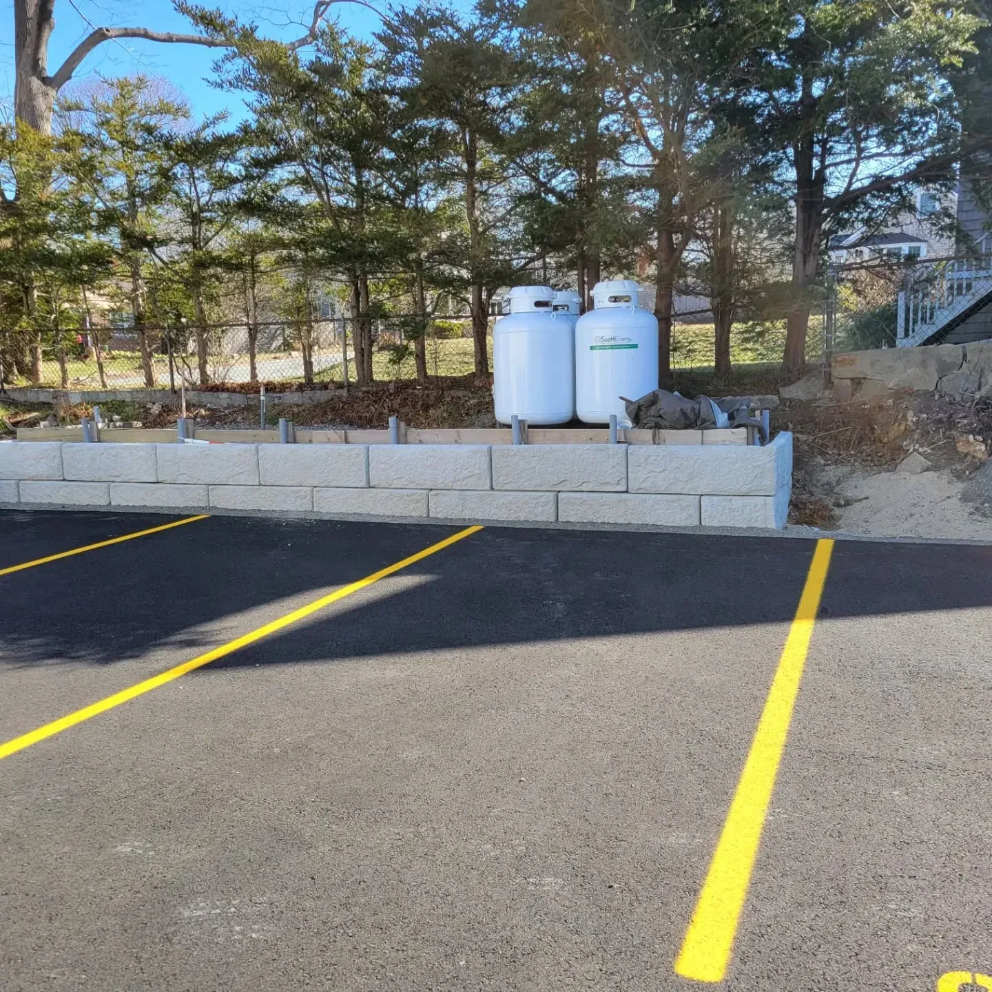 Parking lot with yellow lines, concrete retaining wall, and two white propane tanks in the background.