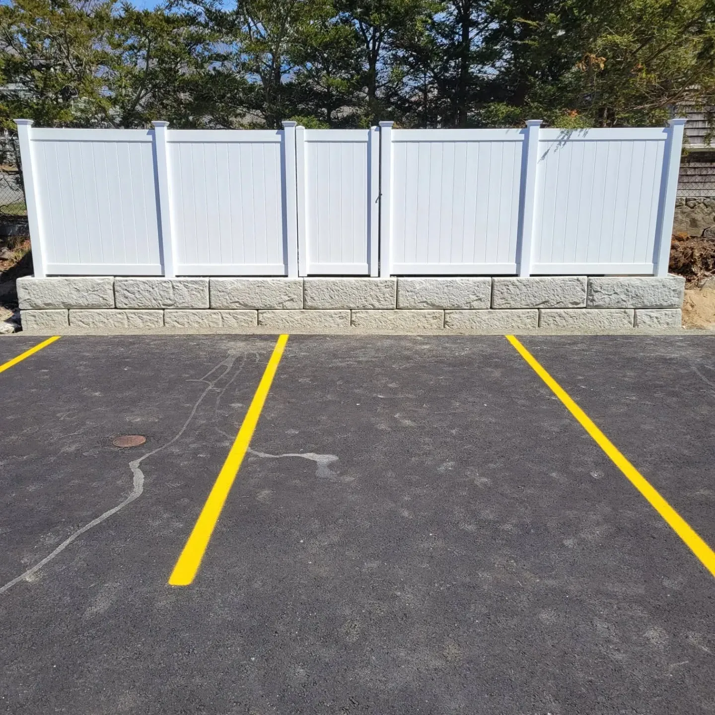 White fence atop a retaining wall, bordering a paved parking area with yellow lines.