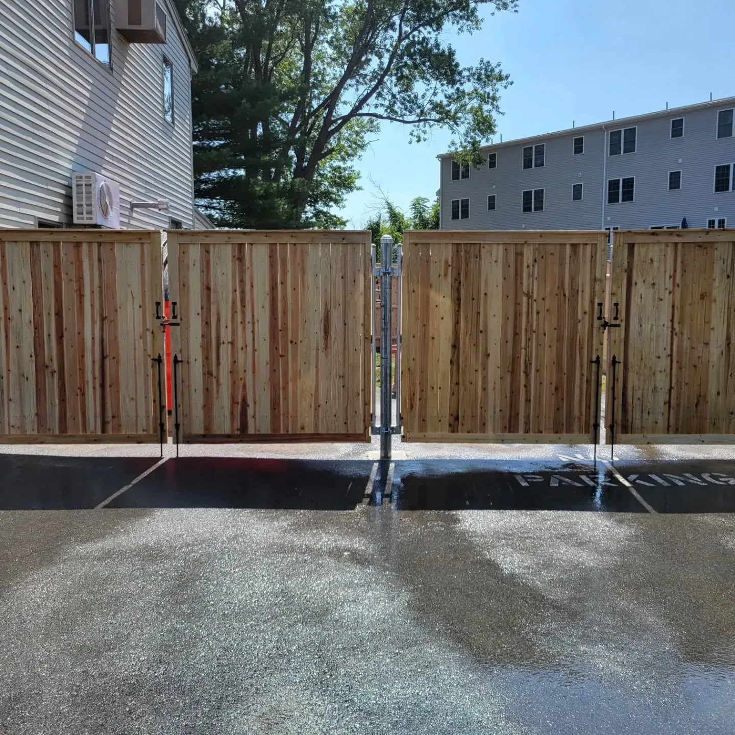 Wooden fence with a gate, wet pavement in front. Buildings in background.