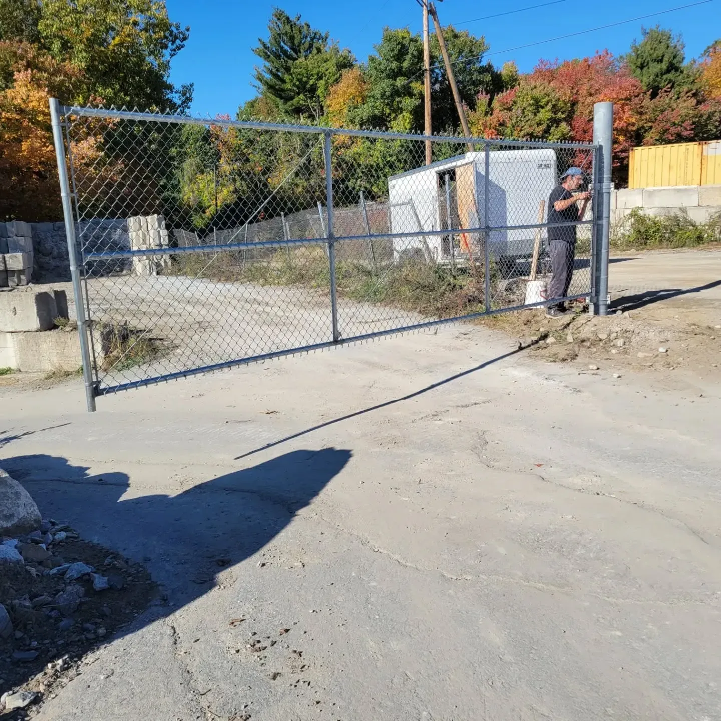 A person by a chain-link gate. They appear to be installing or inspecting the gate, with a shovel nearby.