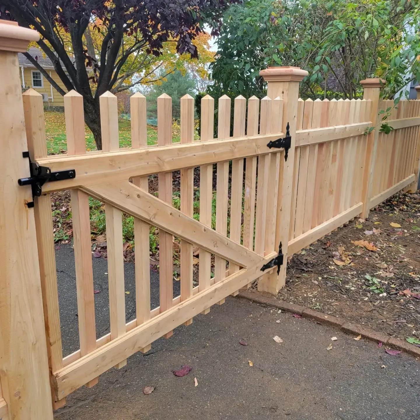 Wooden fence with a gate, in a residential setting. Brown wood, black hardware.