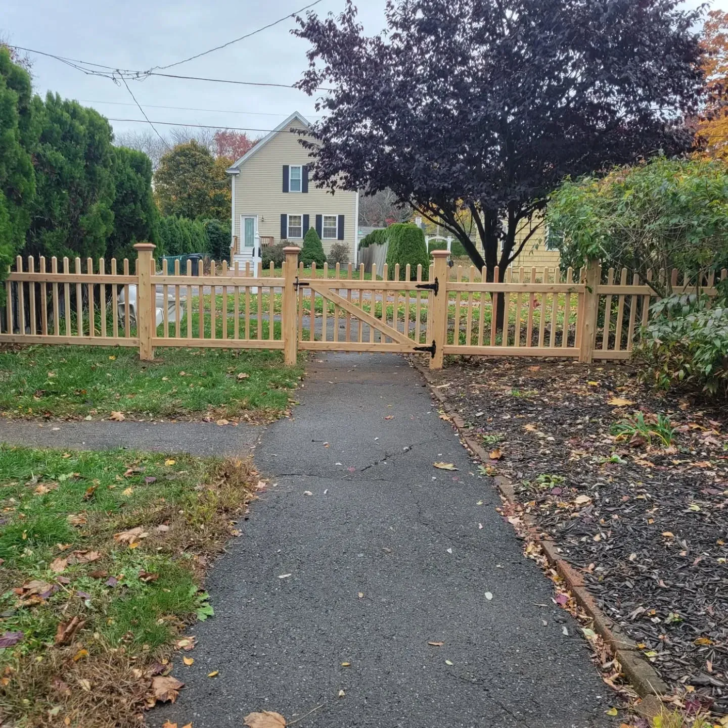 A wooden picket fence with a gate surrounds a front yard, a path leads to the gate.