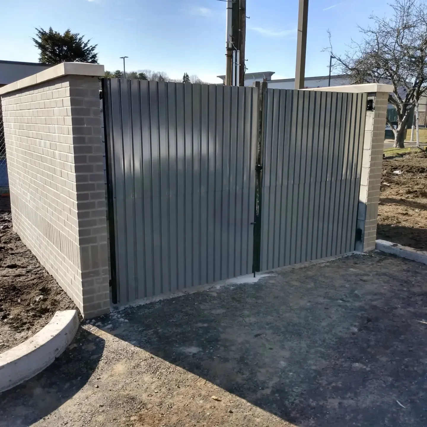 Brick pillars and gray metal gate enclosing a small area, on a concrete surface.