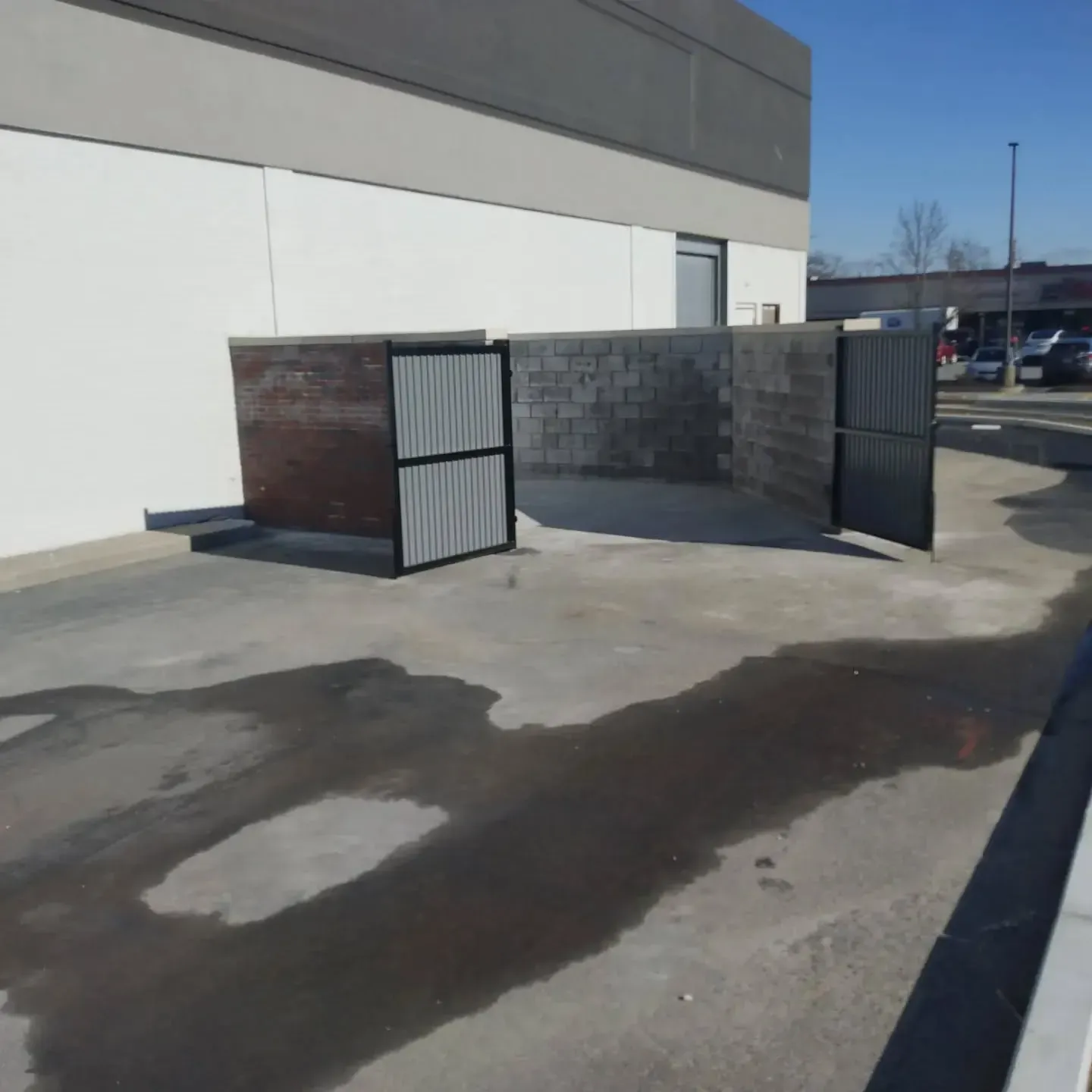 Enclosure for dumpsters with two gray metal gates, concrete walls, and a wet concrete ground.