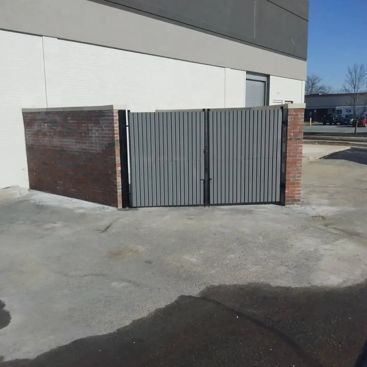 Gray vertical slat gate between brick walls, in front of a building.