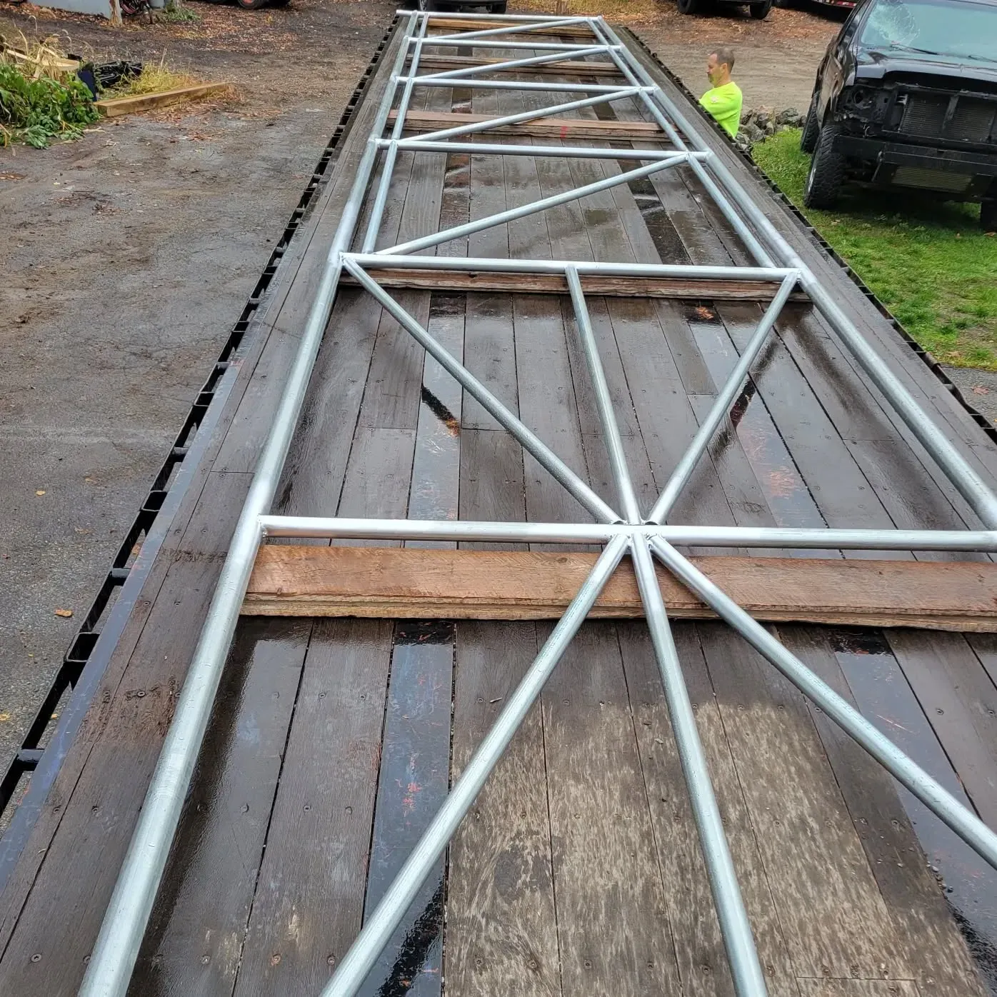 Metal frame structure on a wooden flatbed, likely for transport, with a person in the background.