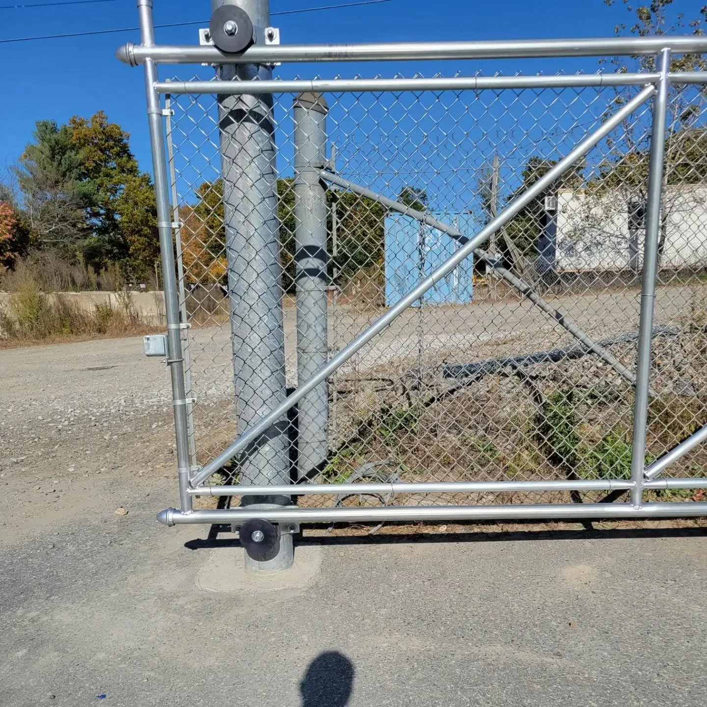 Metal chain-link gate, partially open, with a gray post and a concrete base on a gravel surface.