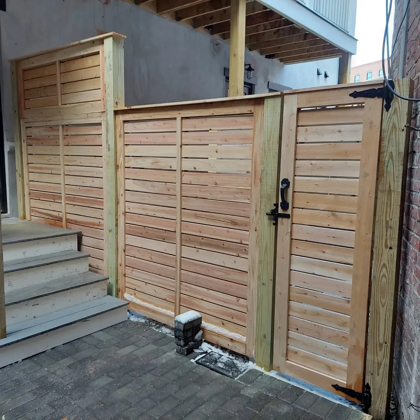 Wooden gate and fence enclose a small brick patio with stairs.