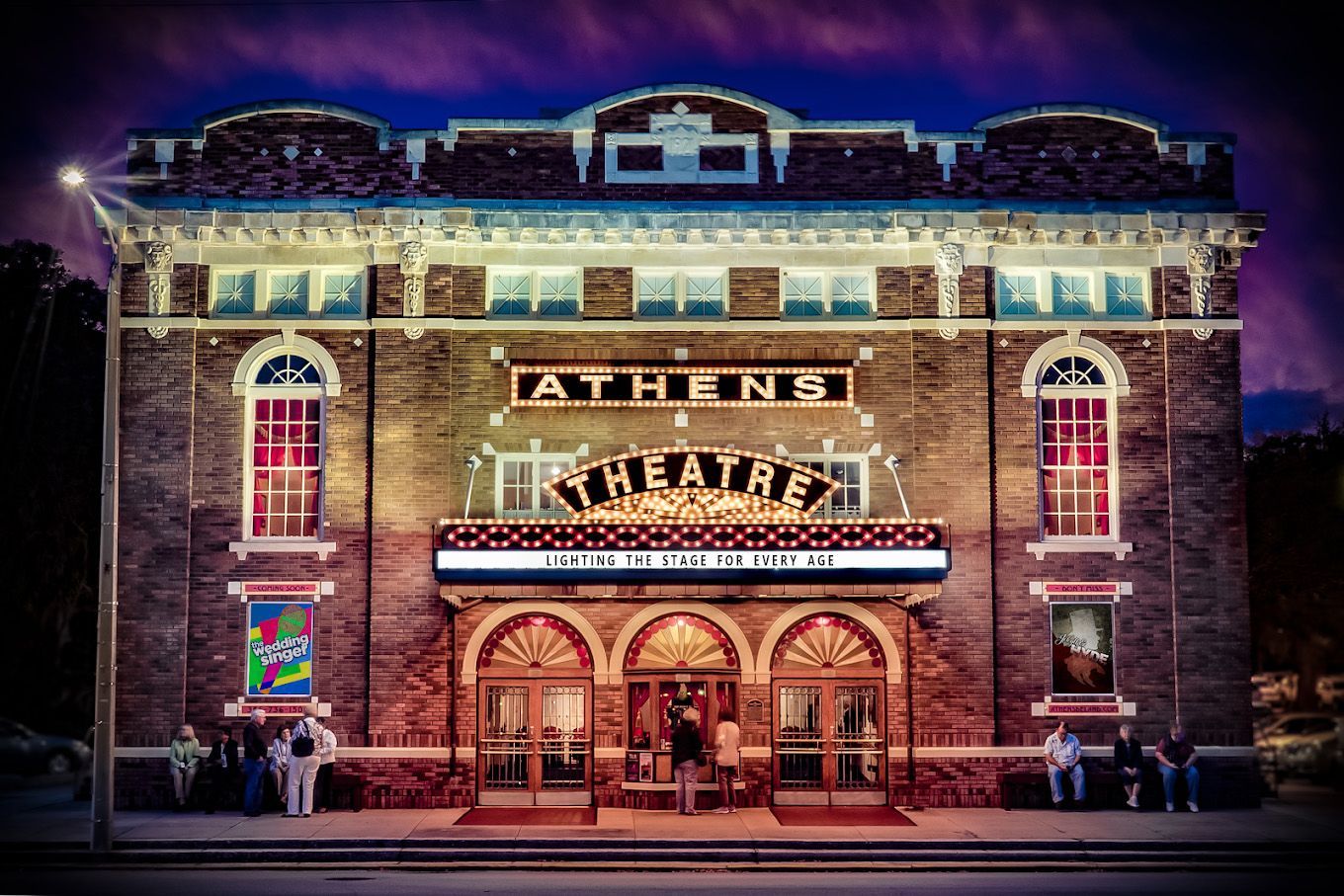A large brick building with a sign that says theatre is lit up at night.