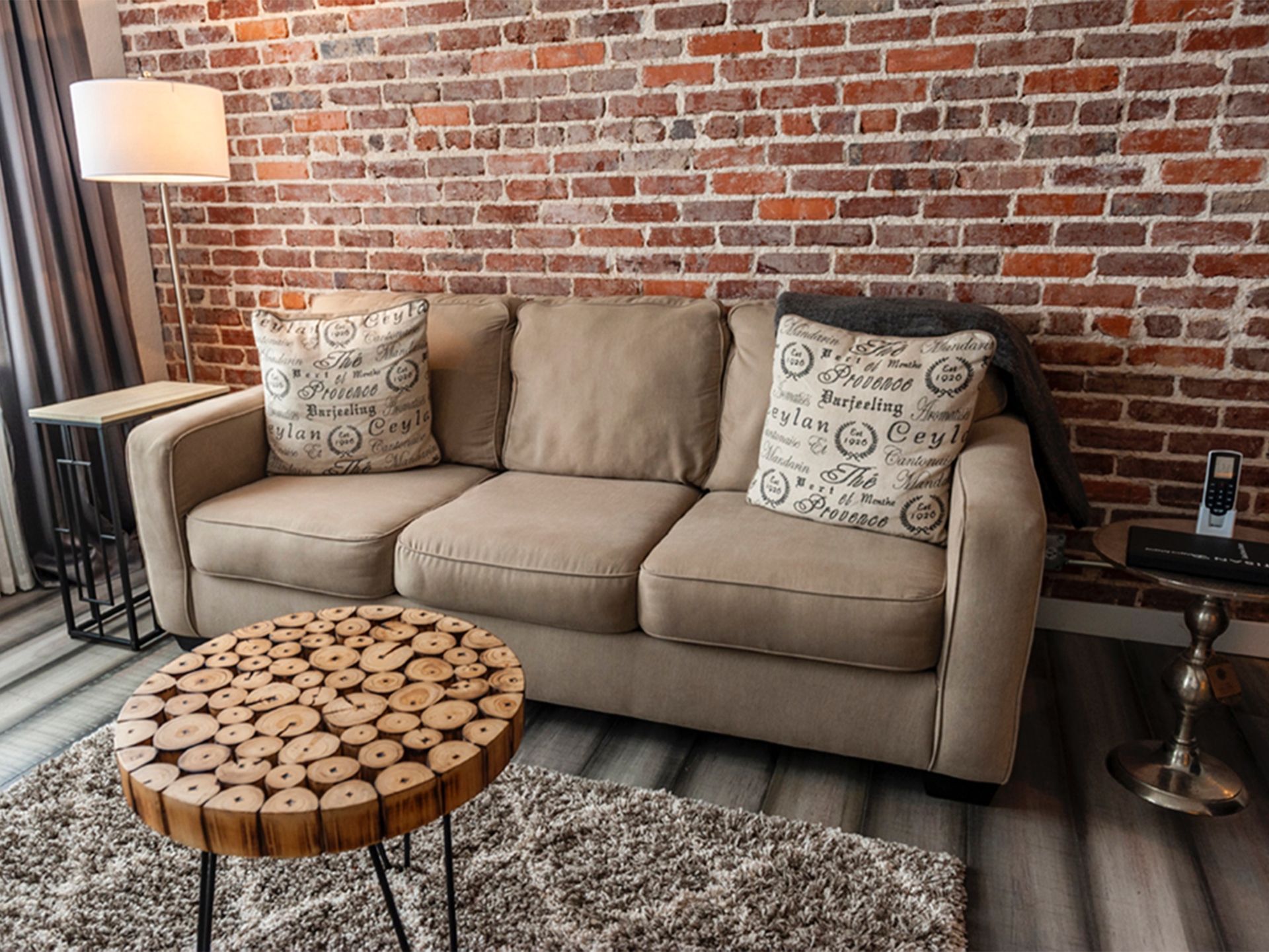 A living room with a couch , table , lamp and brick wall.
