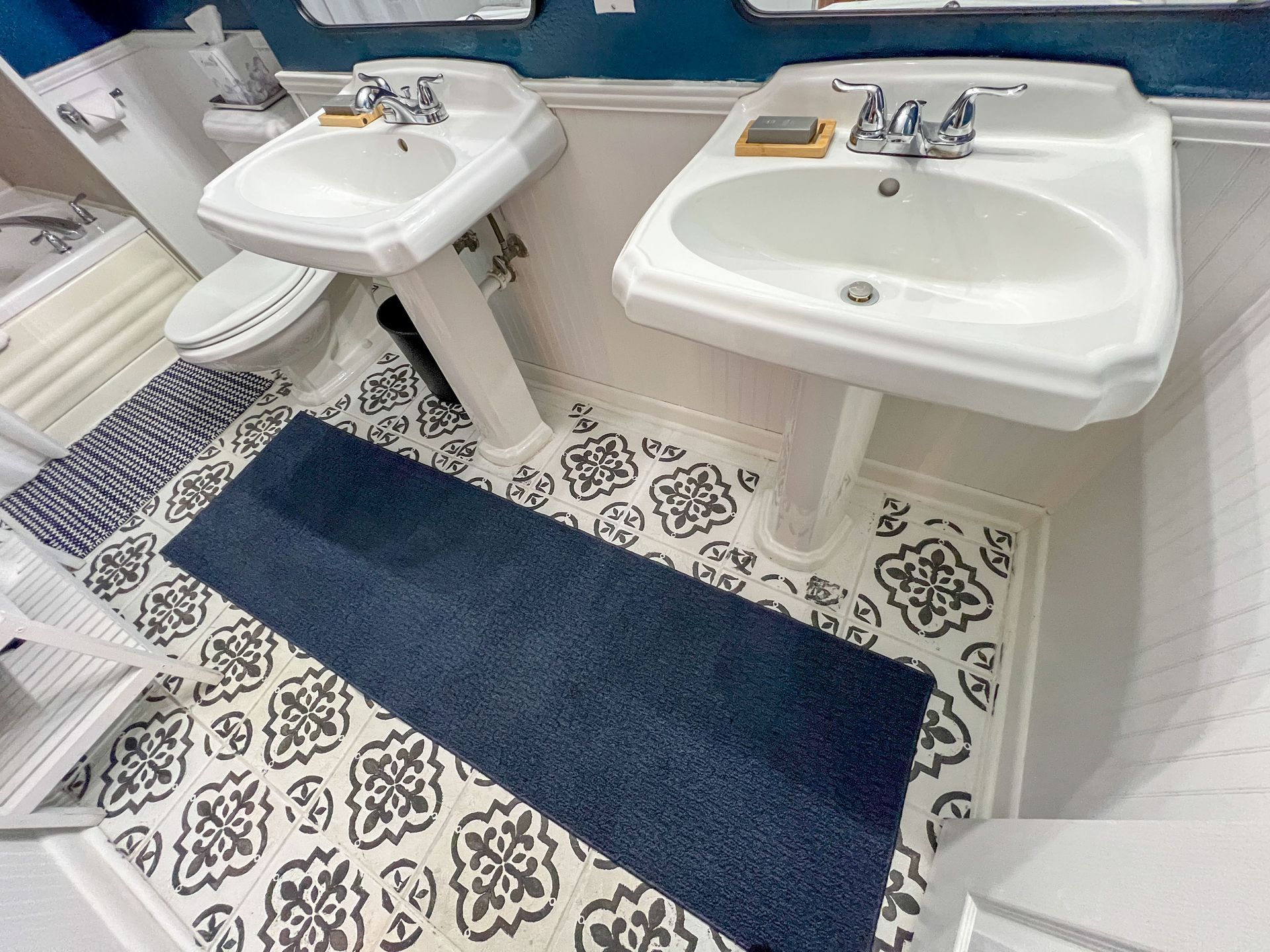 A bathroom with two sinks , a toilet , and a blue rug.