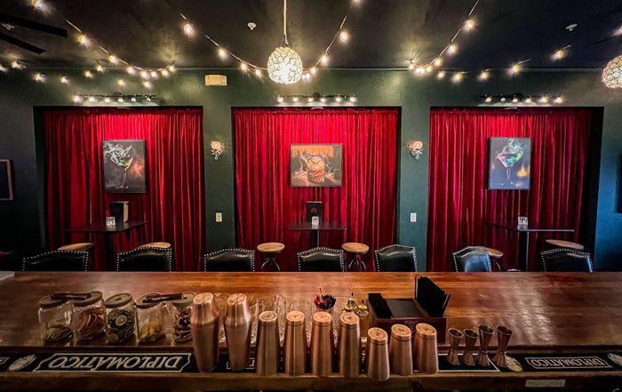 A bar in a restaurant with red curtains and tables.