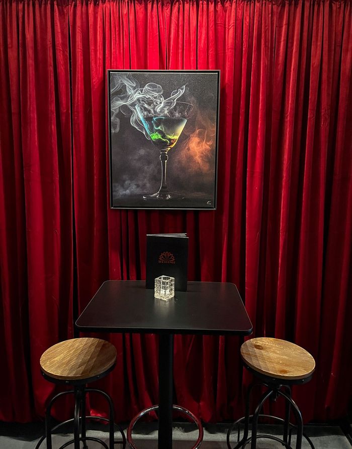 A table and stools in front of a red curtain with a painting of a martini glass on the wall.