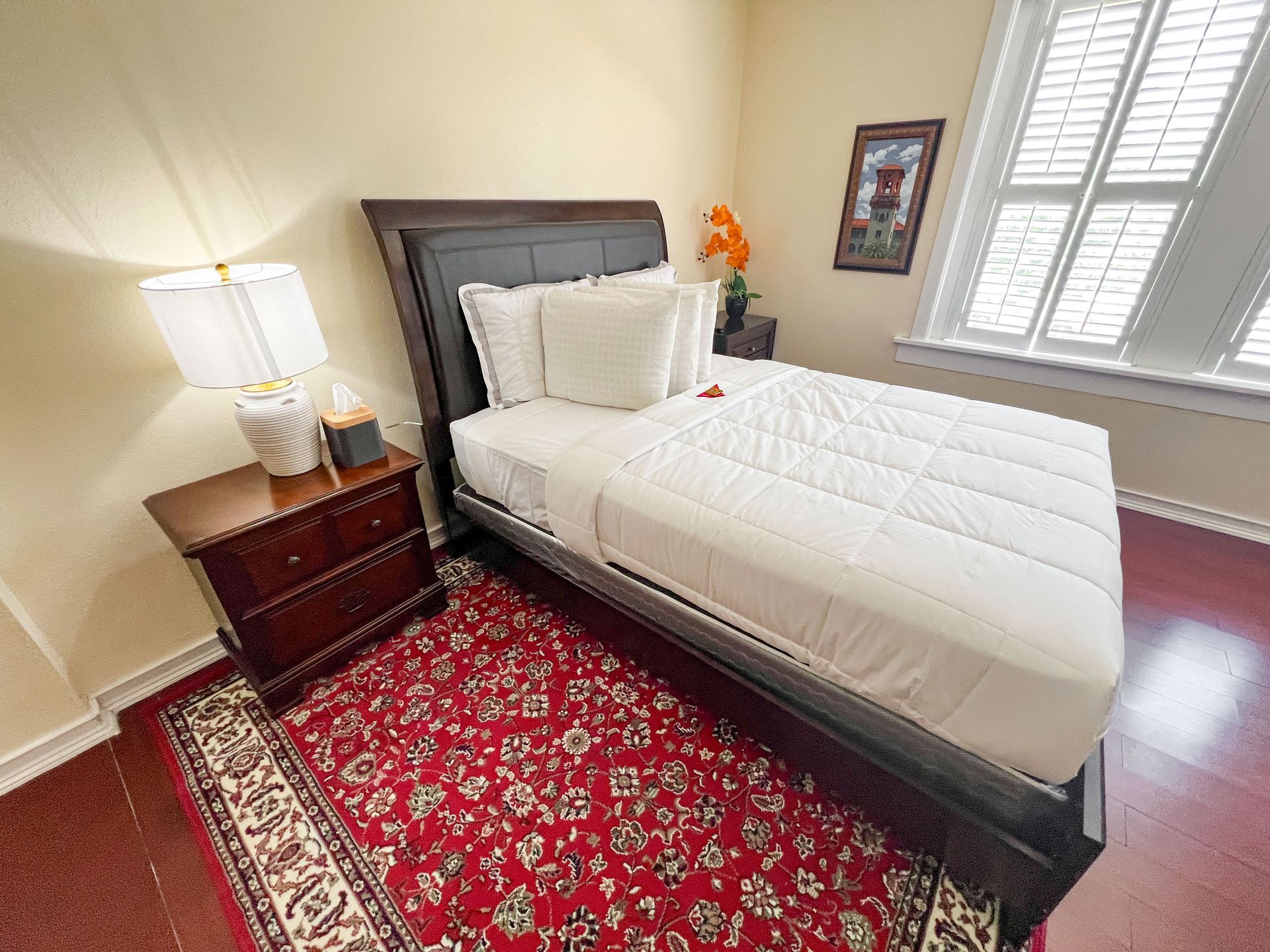A bedroom with a bed , nightstand , lamp and rug.
