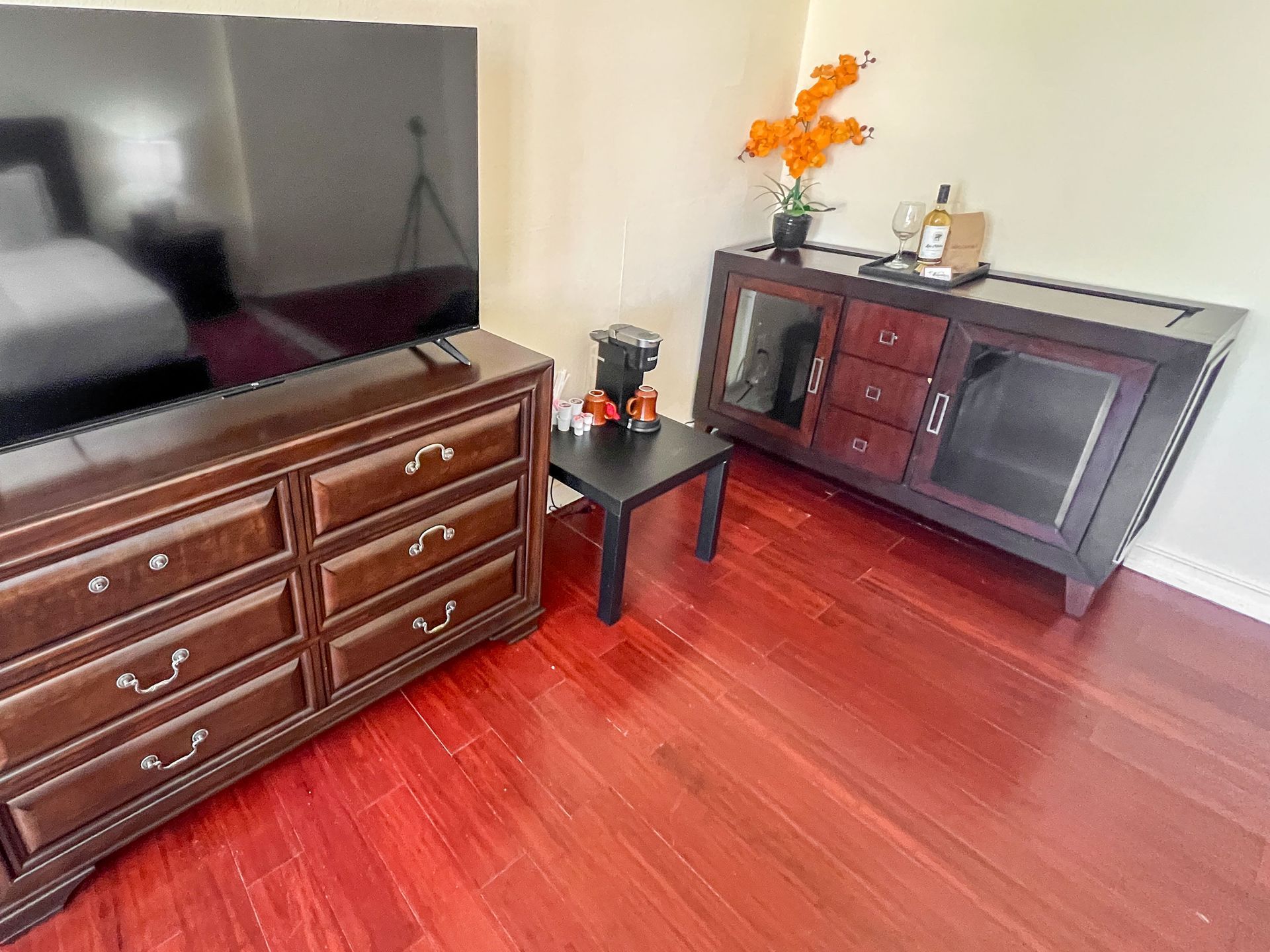 A living room with hardwood floors , a dresser and a flat screen tv.