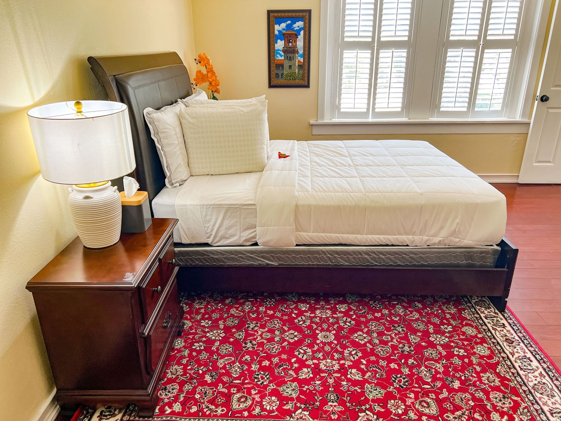 A bedroom with a bed , nightstand , lamp and rug.