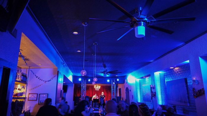 A group of people are sitting in a room with blue lights and a ceiling fan.