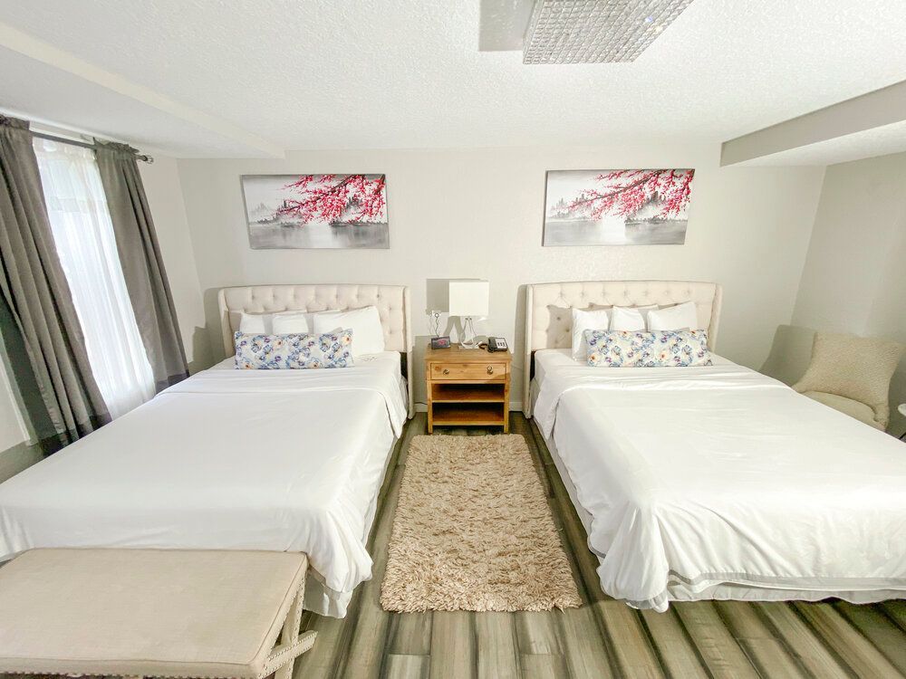 A hotel room with two beds and two nightstands.