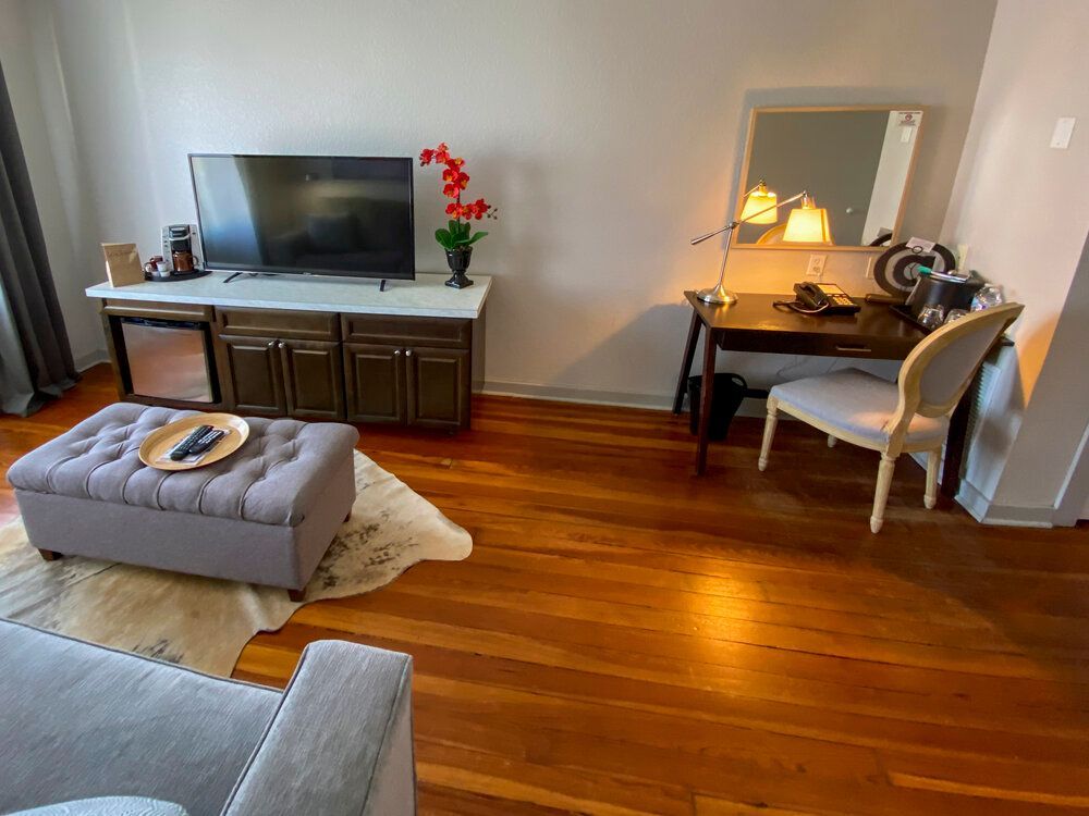 A living room with hardwood floors , a chair , ottoman , desk and television.