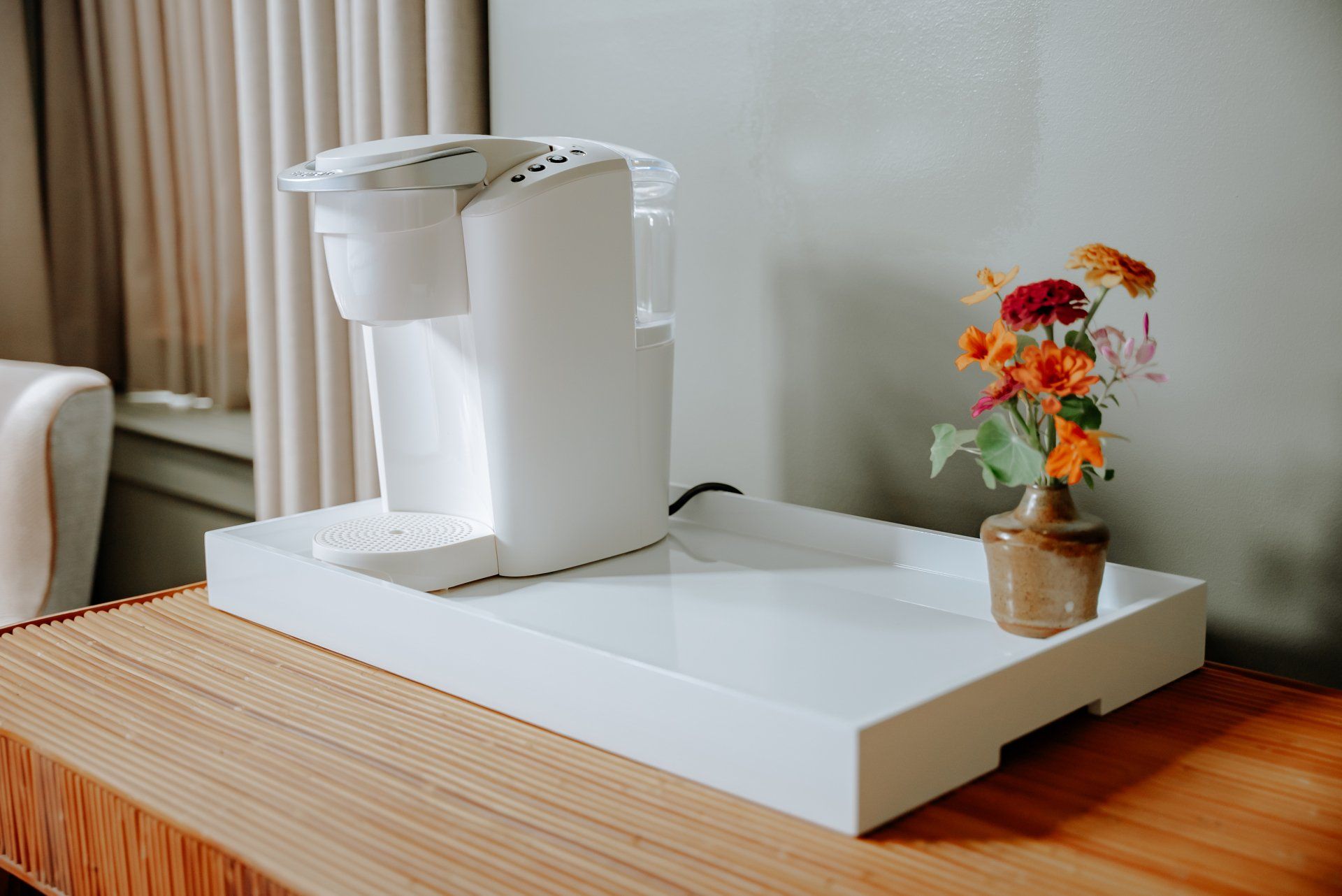A coffee maker is sitting on top of a white tray next to a vase of flowers.