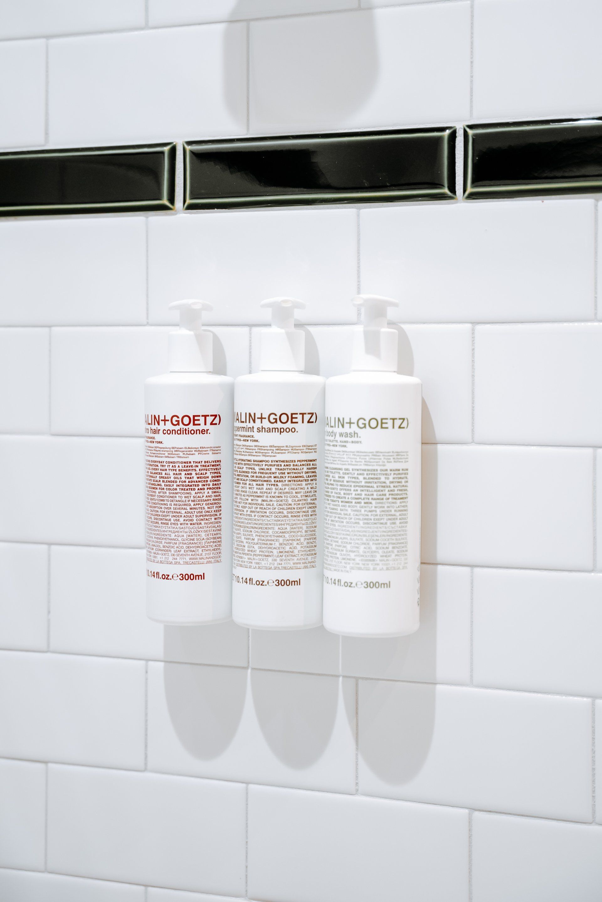 Three bottles of shampoo are hanging on a white tiled wall.