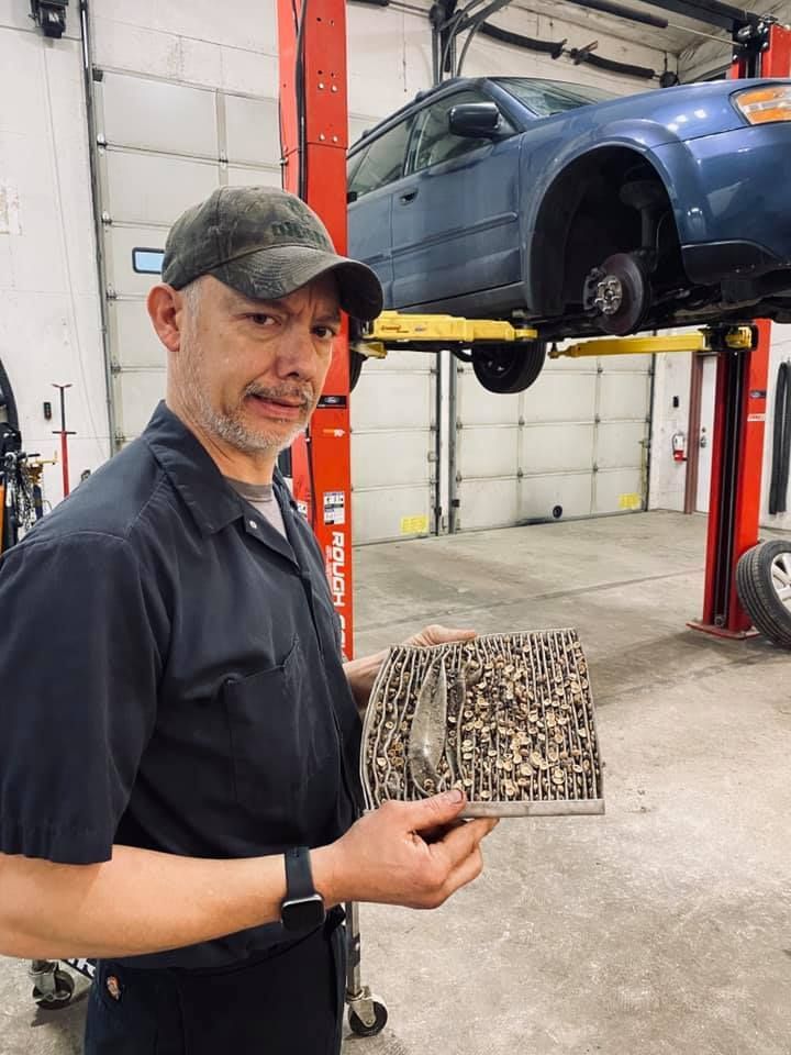 Mechanic holds a severely clogged air filter in auto repair shop. Blue car on lift. | Karraker Mechanical Solutions