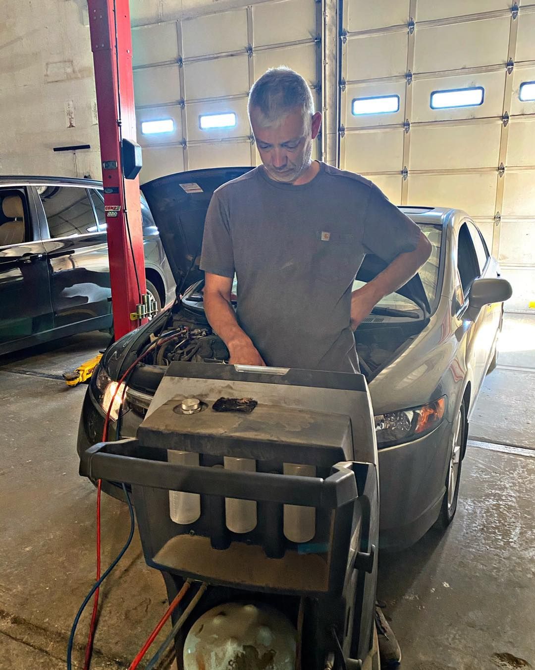 Mechanic inspecting car engine with diagnostic equipment in a garage. Car's hood is open.