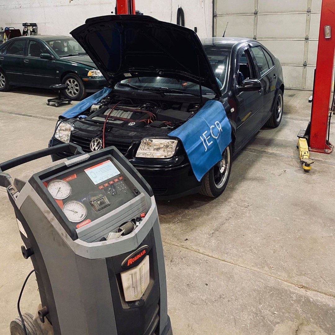 A black car with open hood in a garage being serviced. An AC recharge machine is in the foreground. | Karraker Mechanical Solutions
