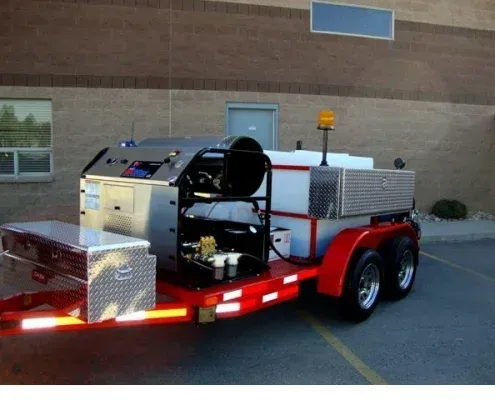 Trailer with machinery for road work, red and silver, parked outside a building.