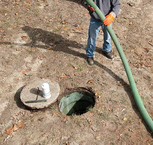 Person emptying septic tank with green hose in yard.