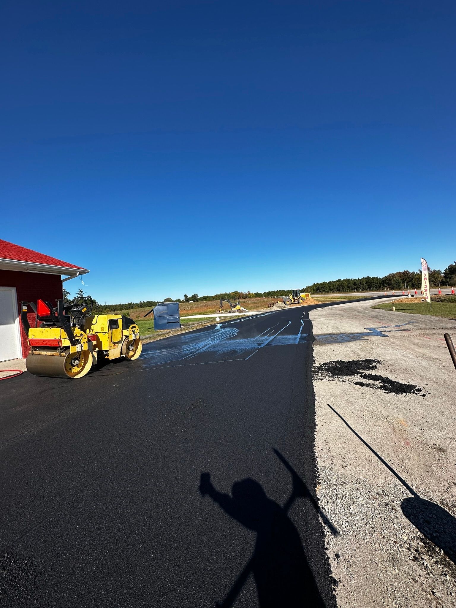 Yellow pickup at a roadside worksite beside a red-roofed building under a clear blue sky