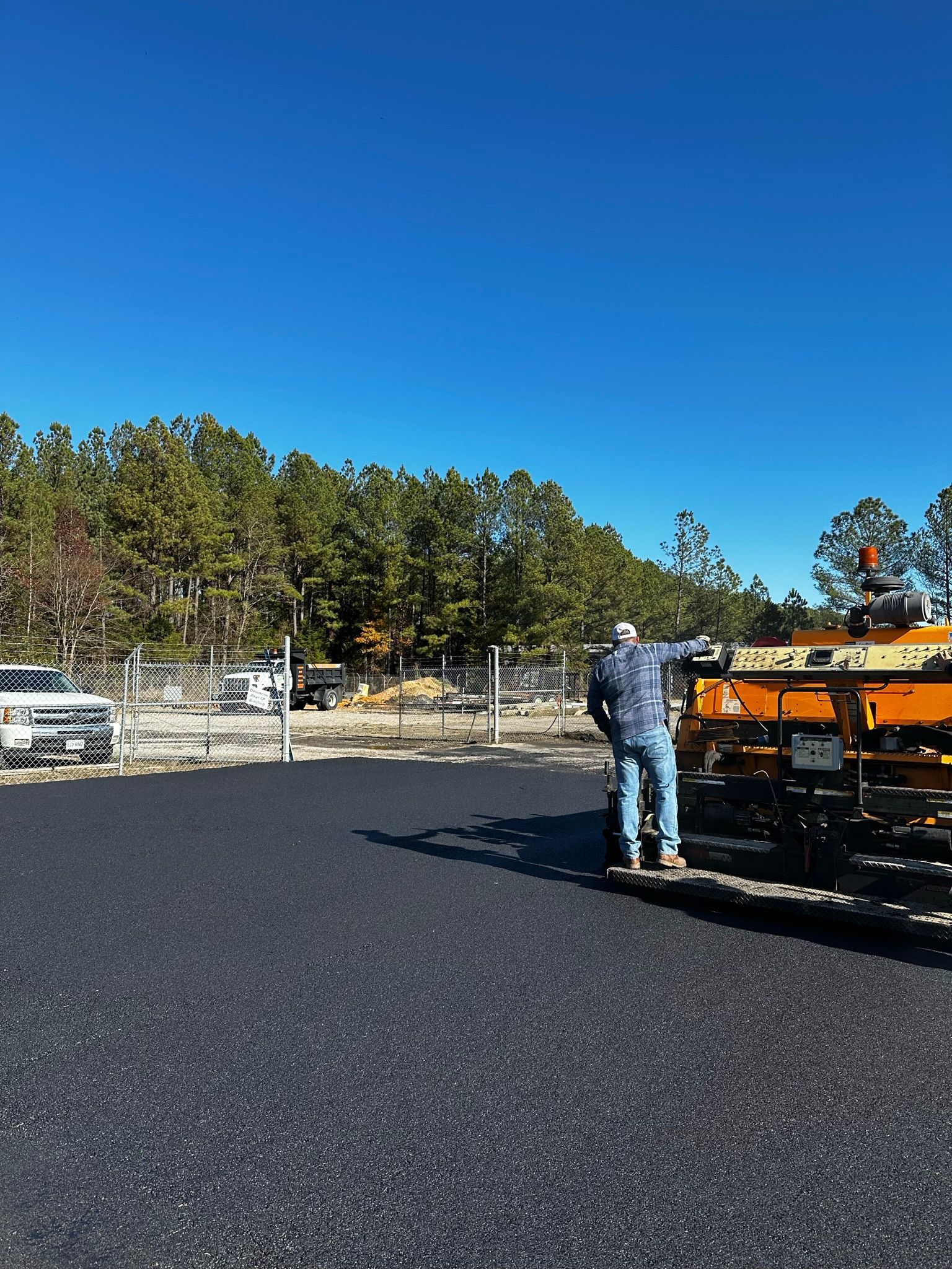 Worker at a road construction site beside an orange paver under a clear blue sky