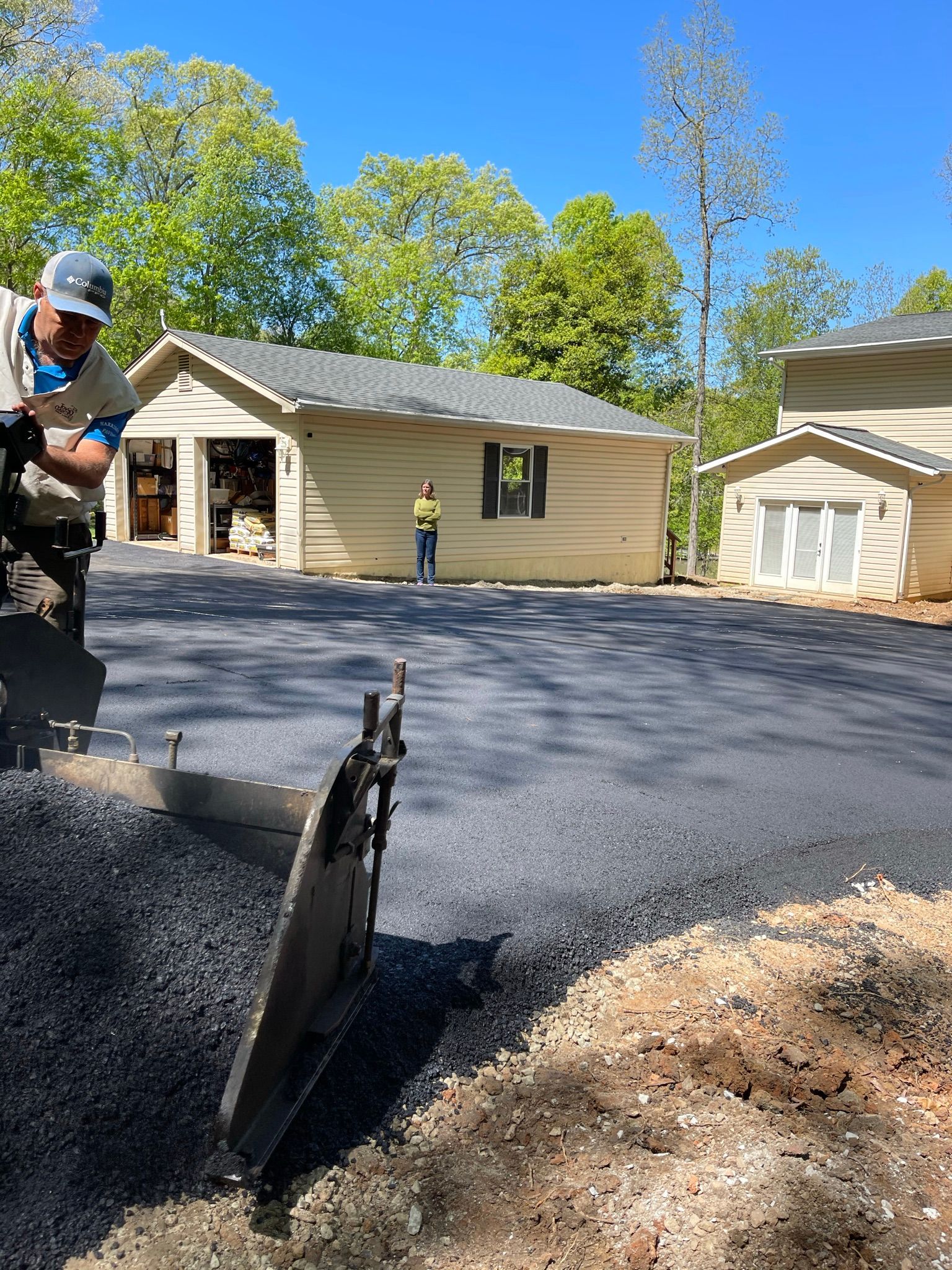 Workers paving a driveway with fresh black asphalt outside a beige house on a sunny day