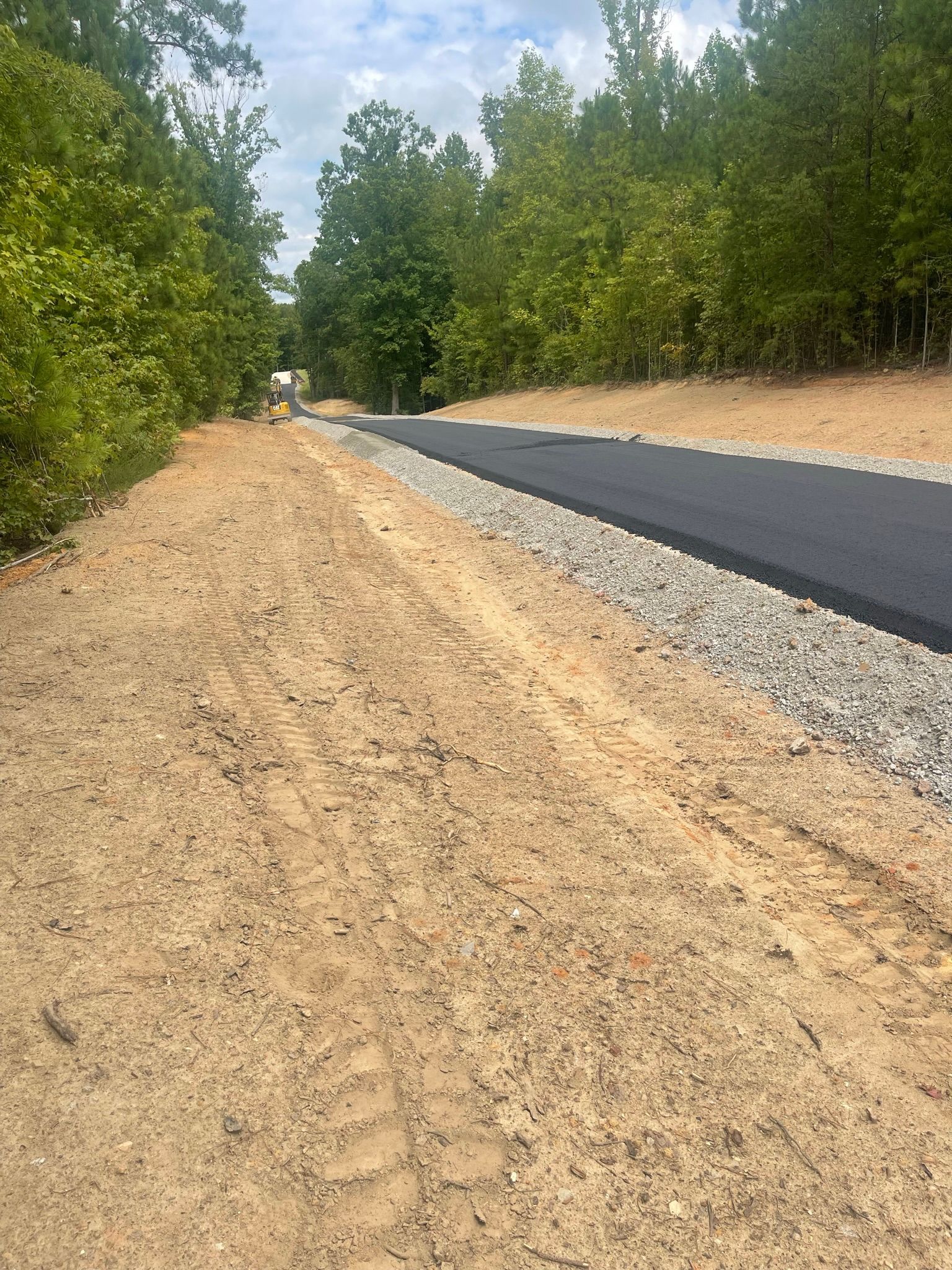 New asphalt road under construction beside gravel shoulder and trees