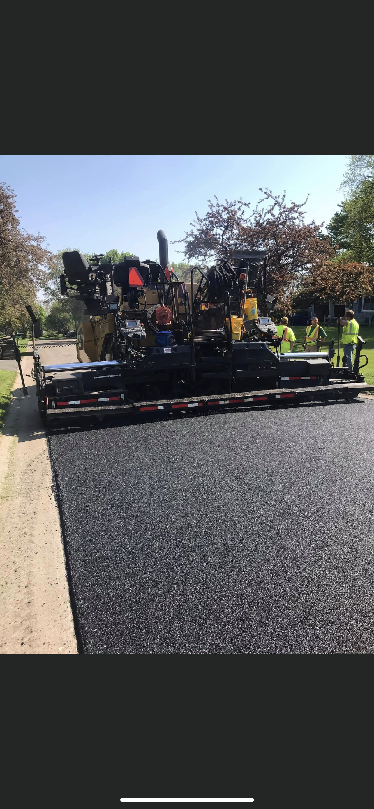 Road paving machine on a street with workers nearby, laying fresh black asphalt in daylight