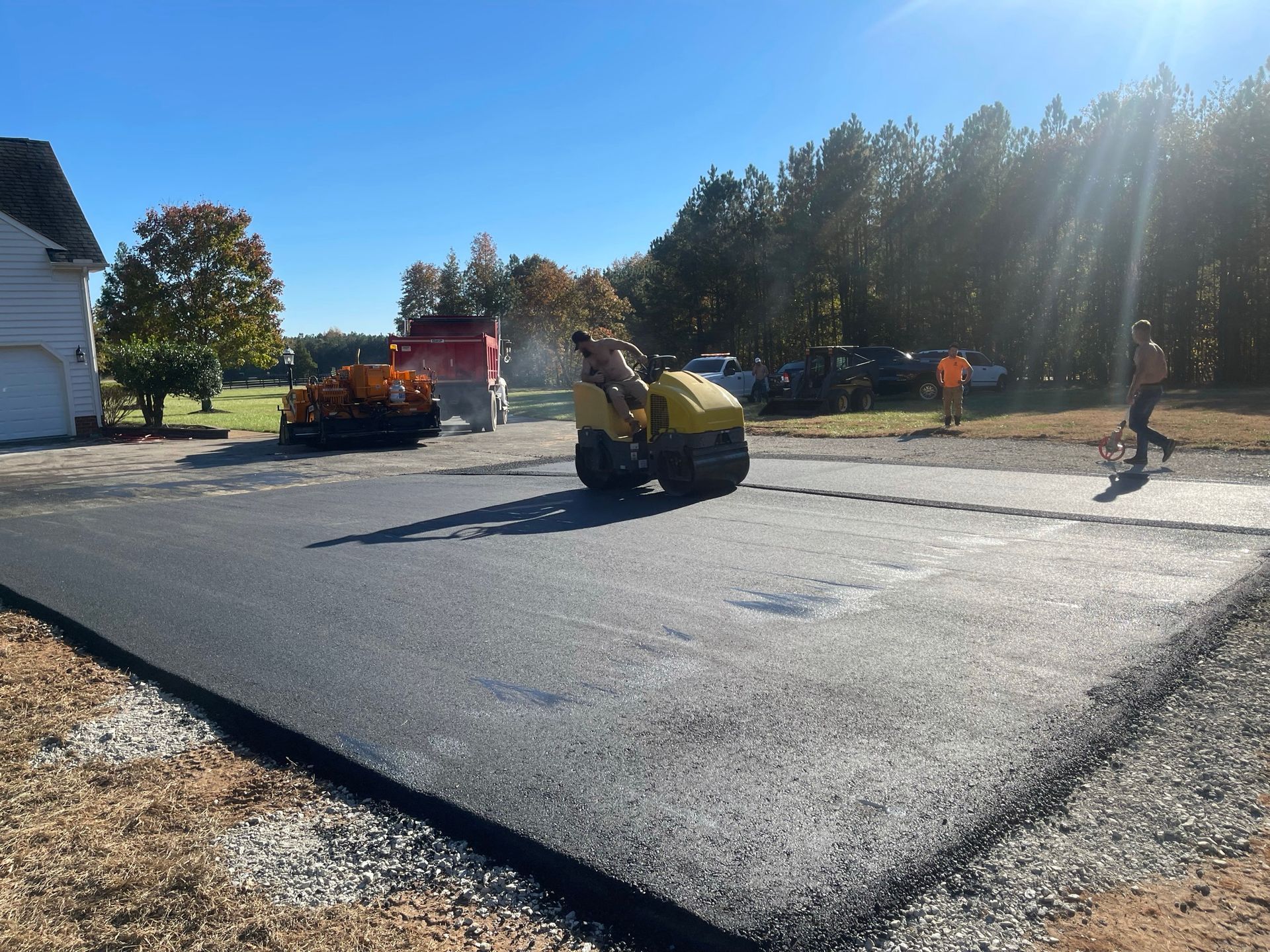 Road paving crew using a roller on a residential street in bright sunlight