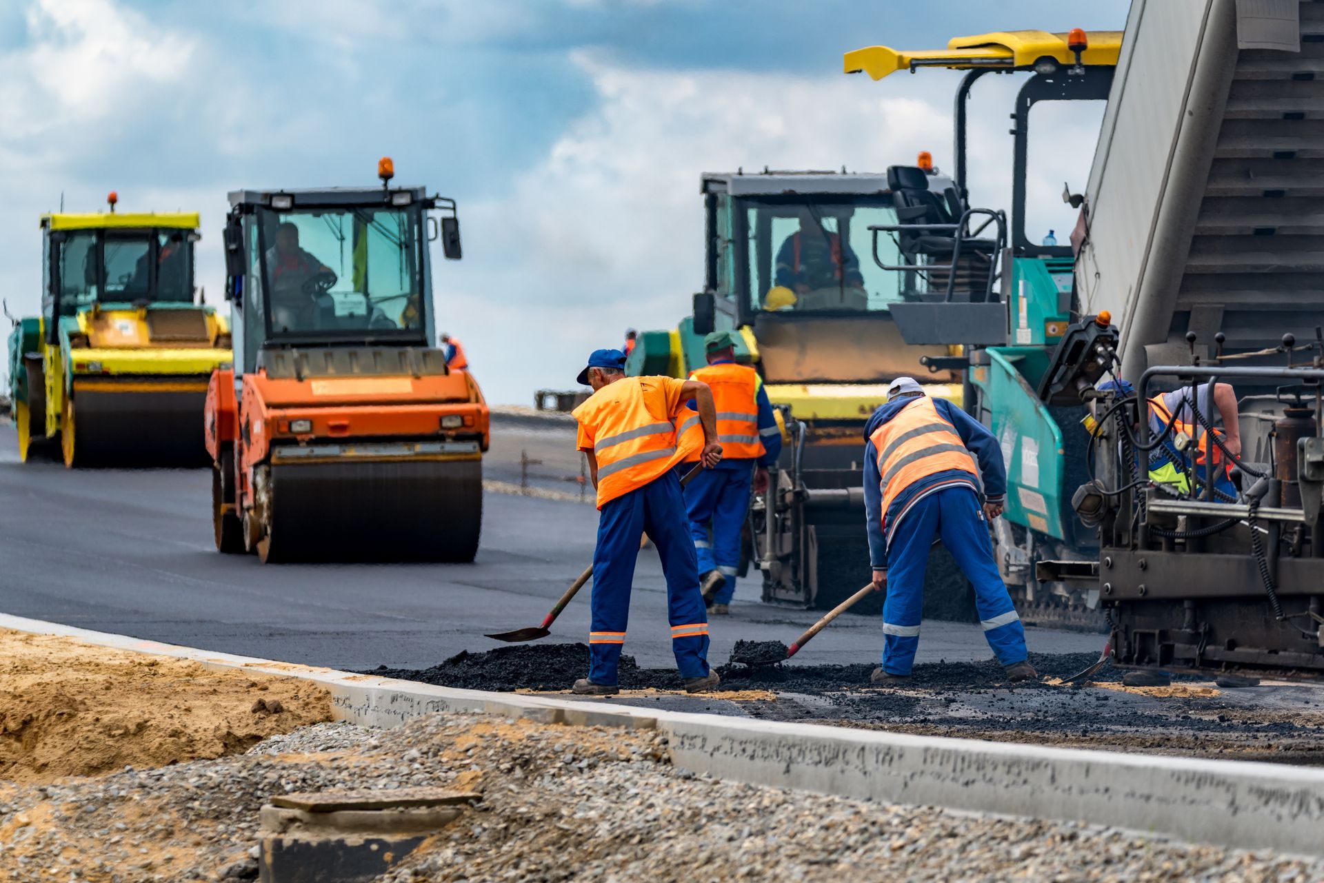 Road crew paving asphalt near heavy construction vehicles and a dump truck