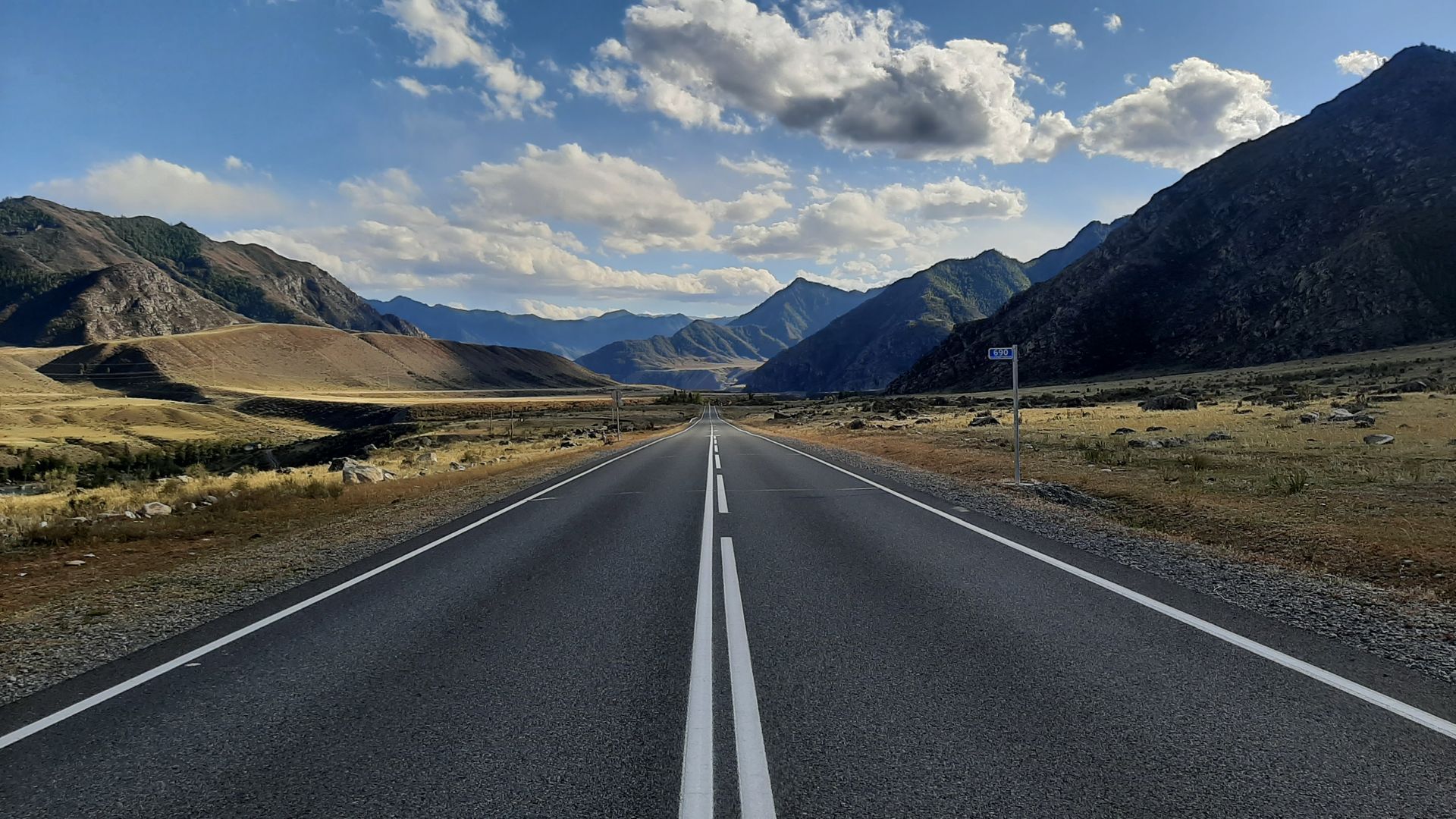 Empty highway stretching toward mountains under a cloudy blue sky