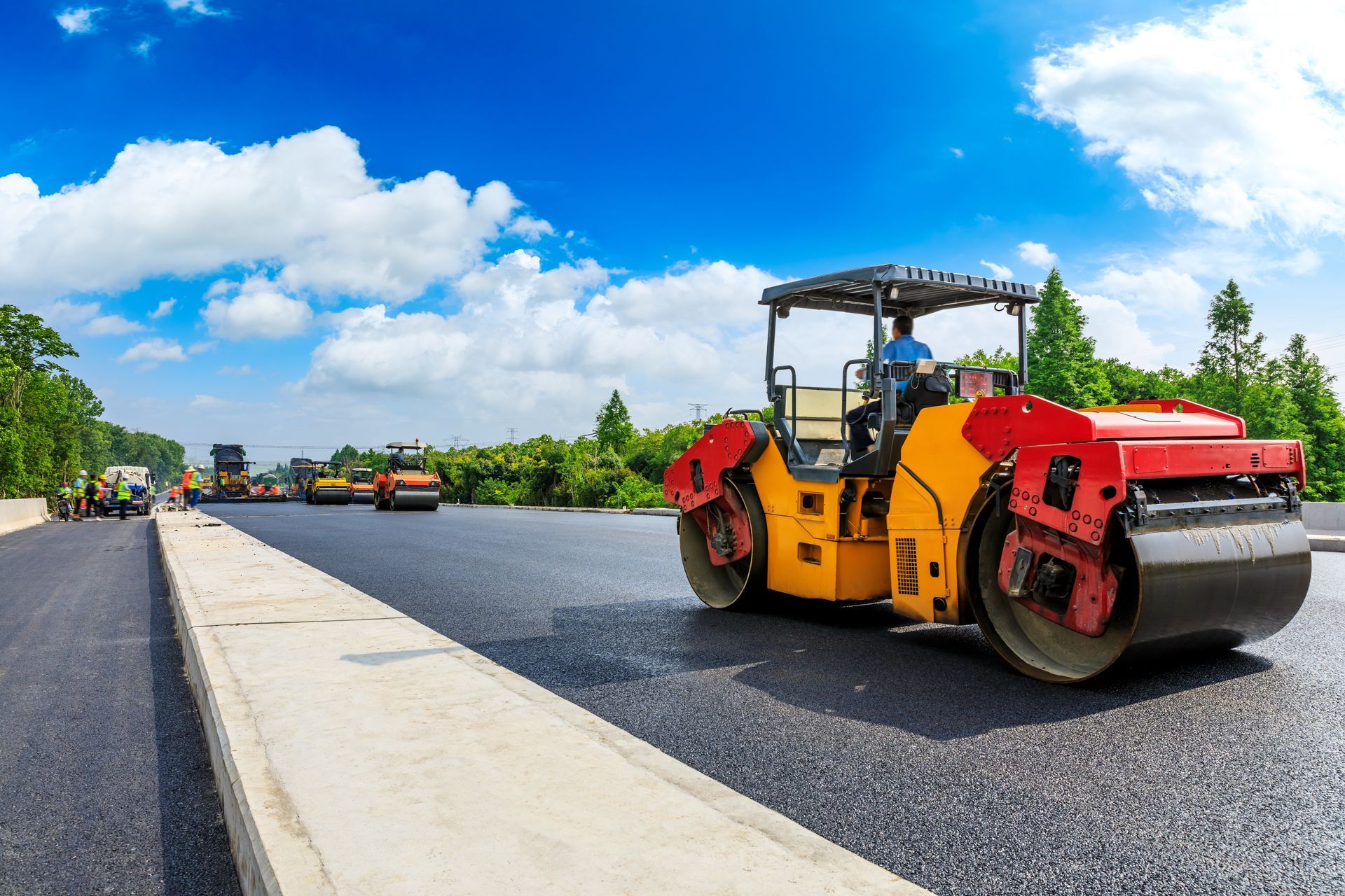 Road roller paving a new asphalt street beside a curb under a blue sky