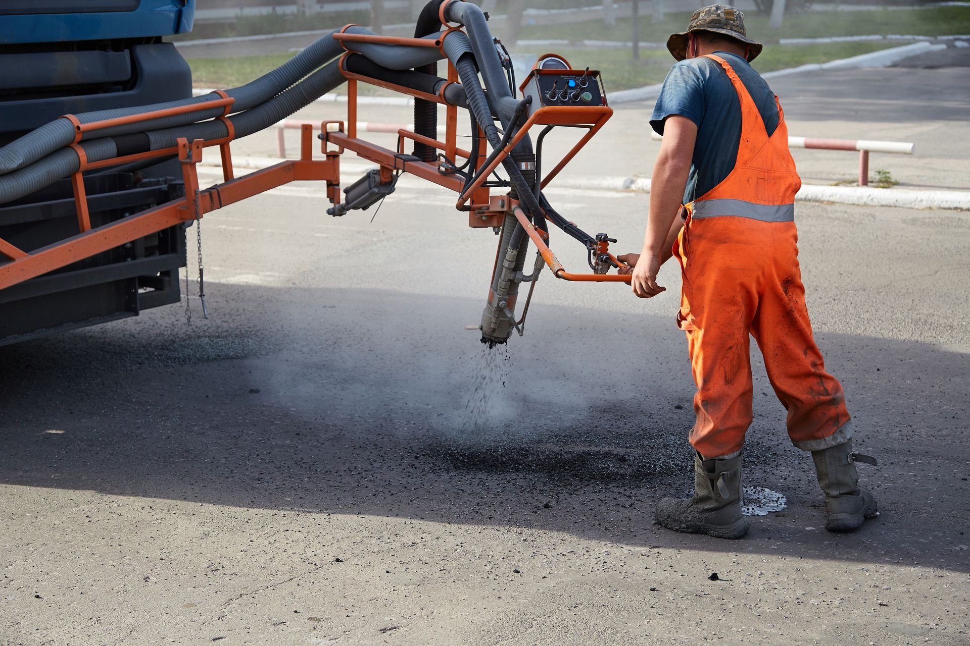 Road worker in orange safety gear spraying black asphalt from a truck-mounted hose