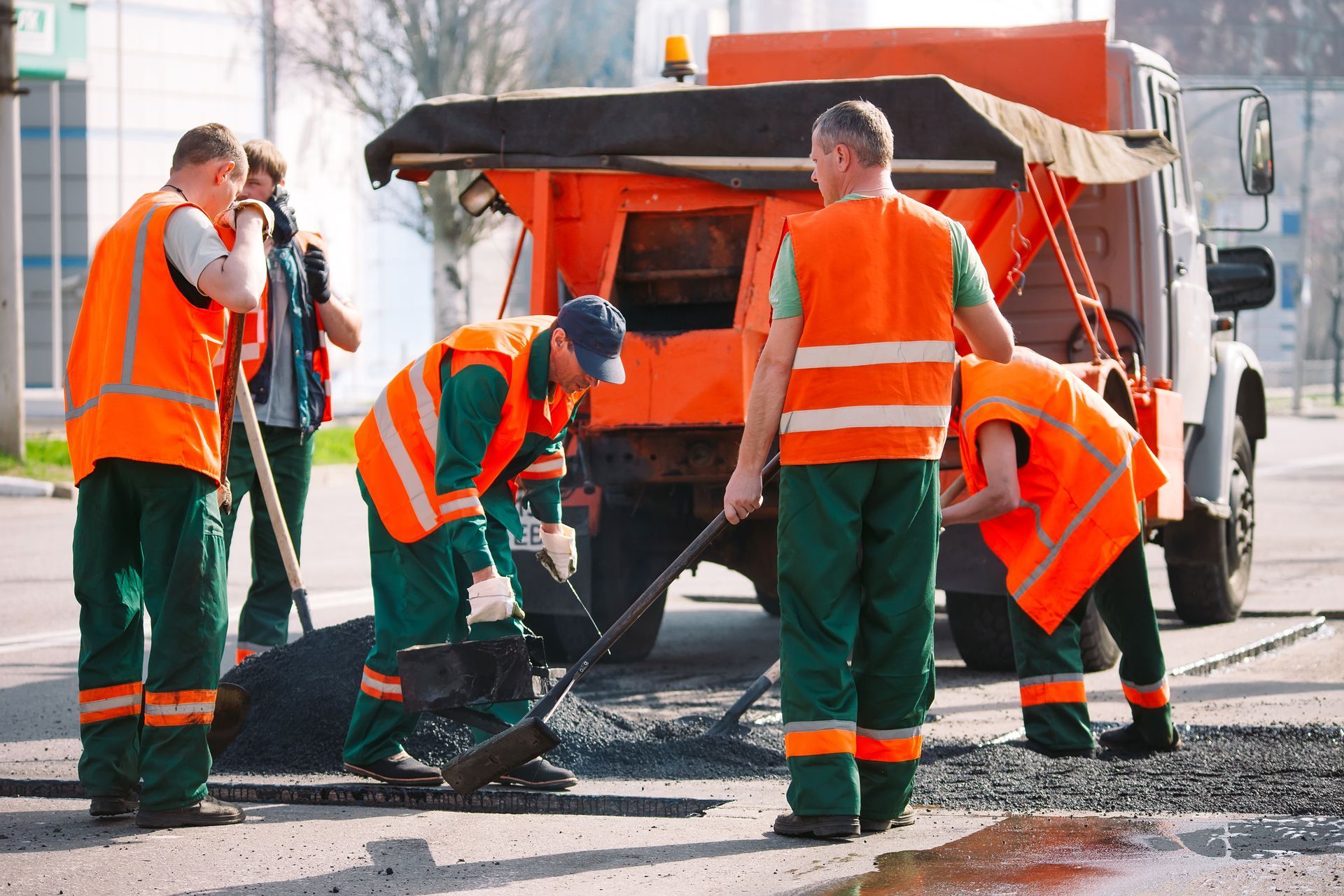 Road workers in orange safety vests repairing a street with a truck and tools nearby