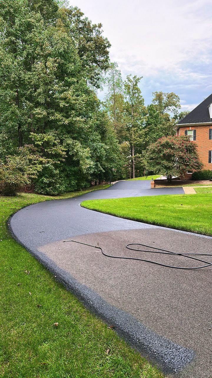 Curved asphalt driveway through green lawn beside trees and a brick house
