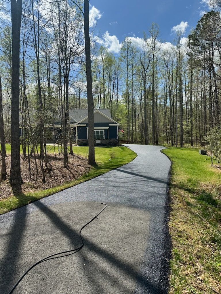 Curved paved path leading to a small green building in a sunny wooded area with tall trees and blue sky